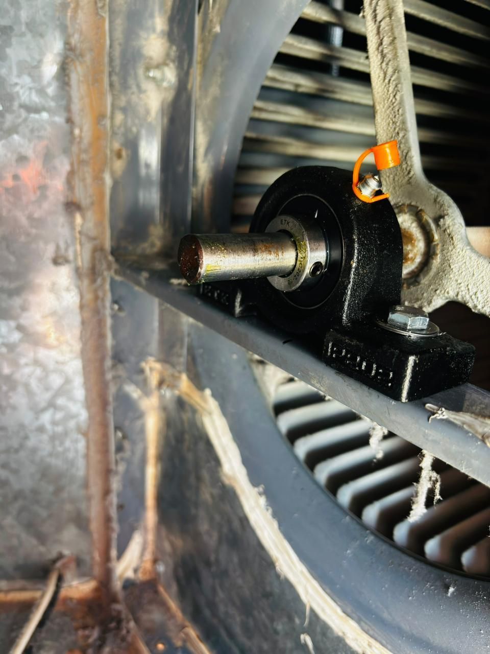 Vista de cerca de un cojinete de soporte metálico con una boquilla de engrase naranja instalada en una barra de soporte metálica.