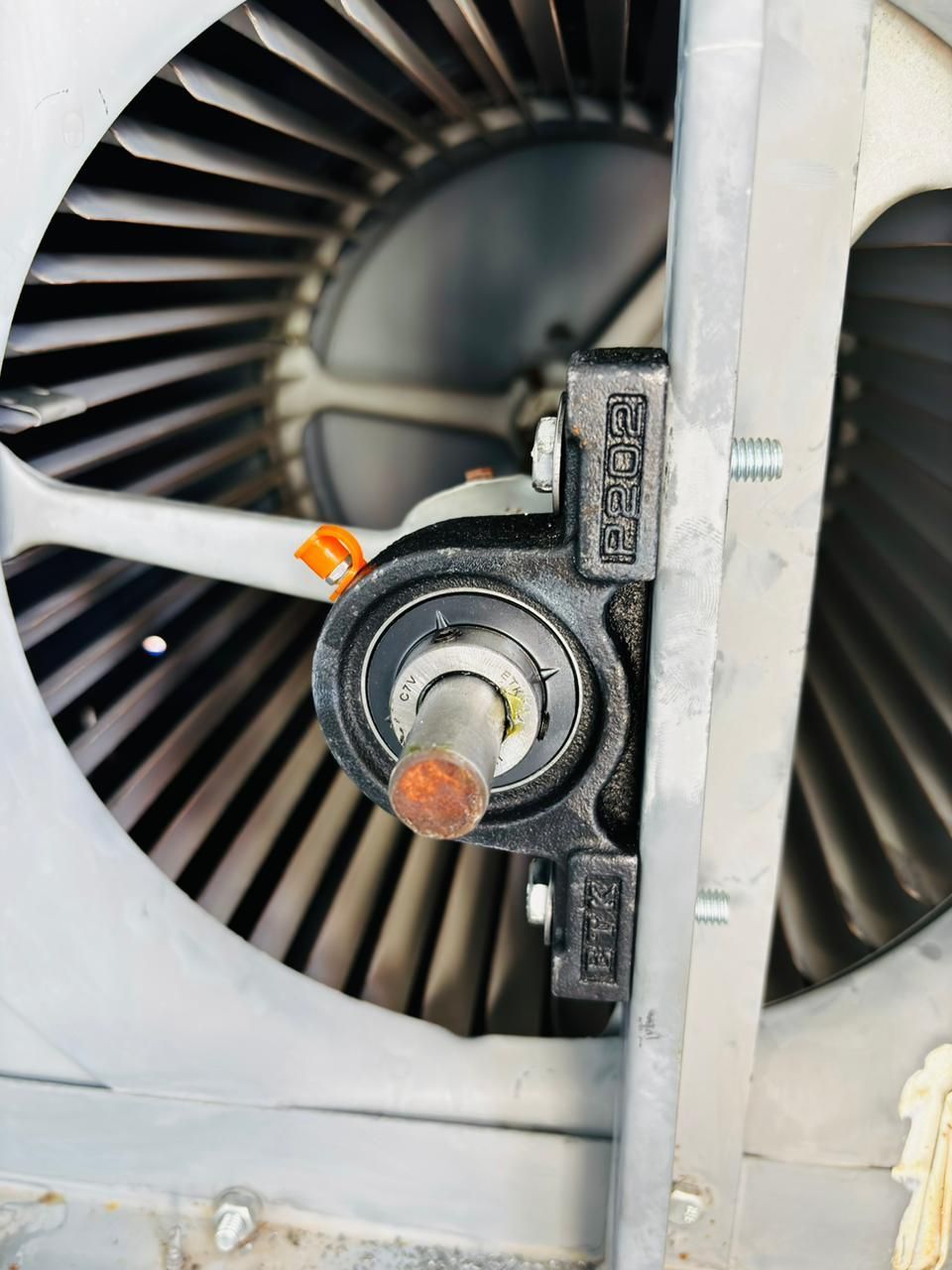 Un cojinete de bloque de almohada negro montado en el brazo de soporte metálico de un ventilador dentro de una unidad de climatización.