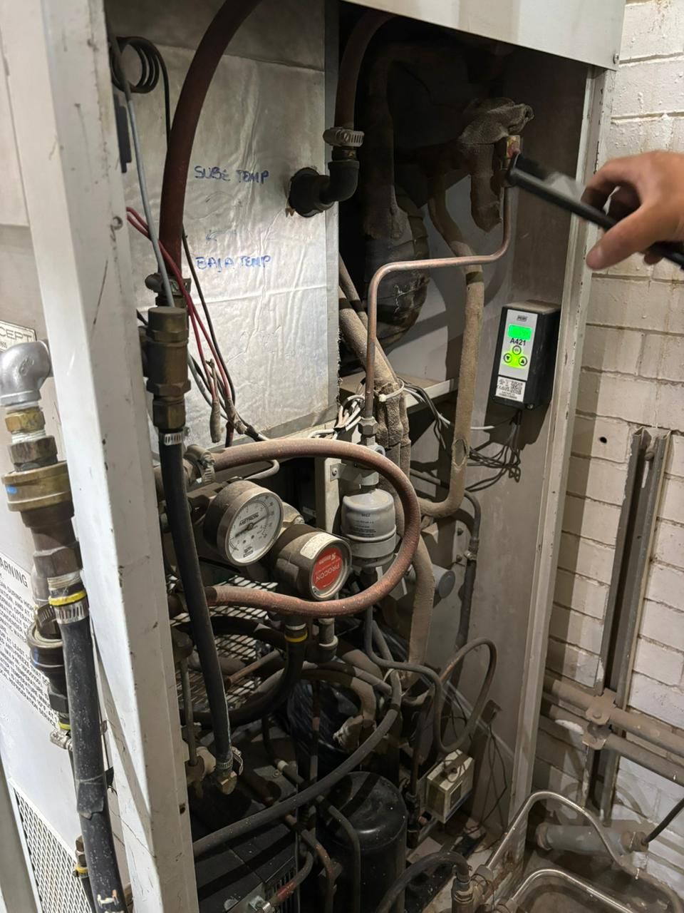 Una persona introduce la mano en un sistema de climatización abierto para inspeccionar las tuberías internas de cobre y los controles digitales.