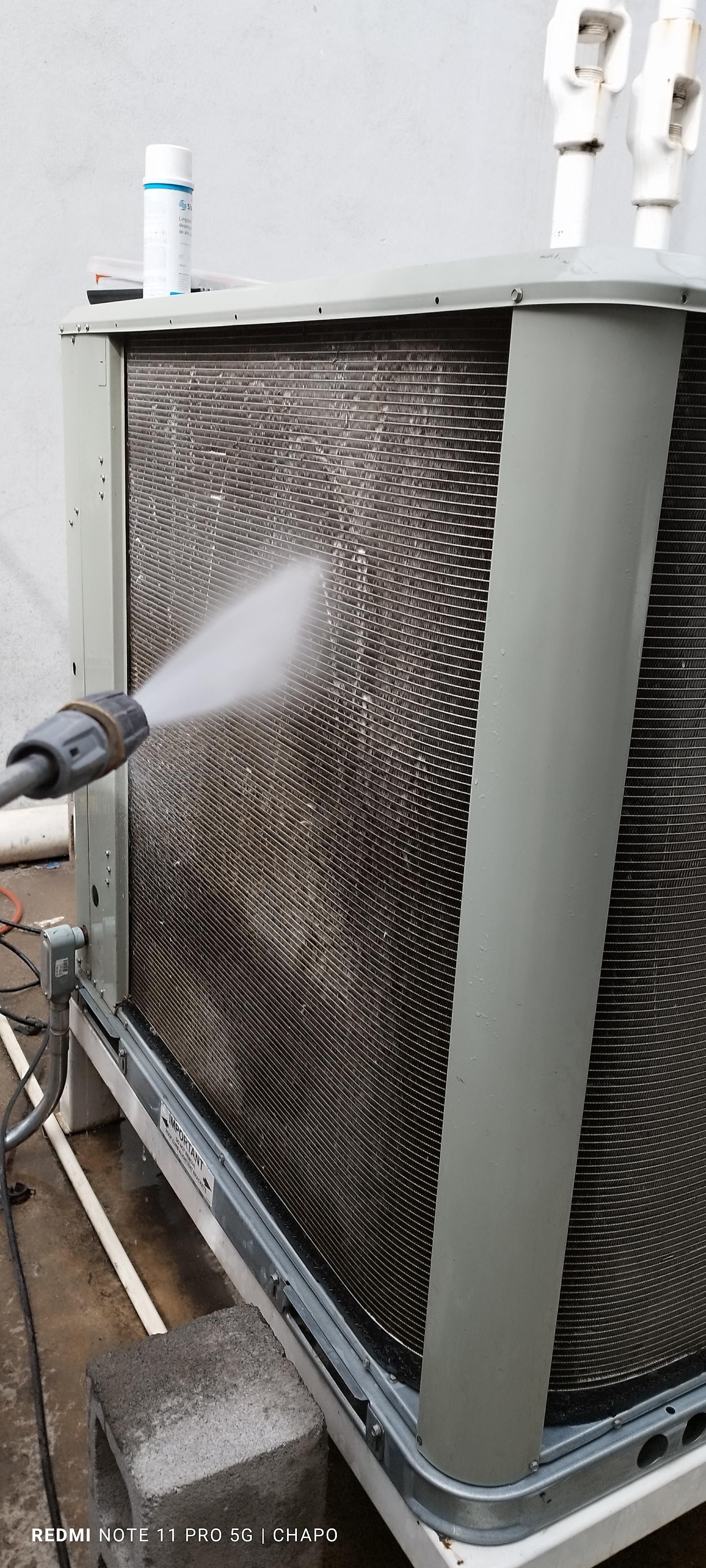 Una boquilla de pulverización de alta presión limpia la suciedad y los residuos de las aletas metálicas de una unidad exterior de aire acondicionado.