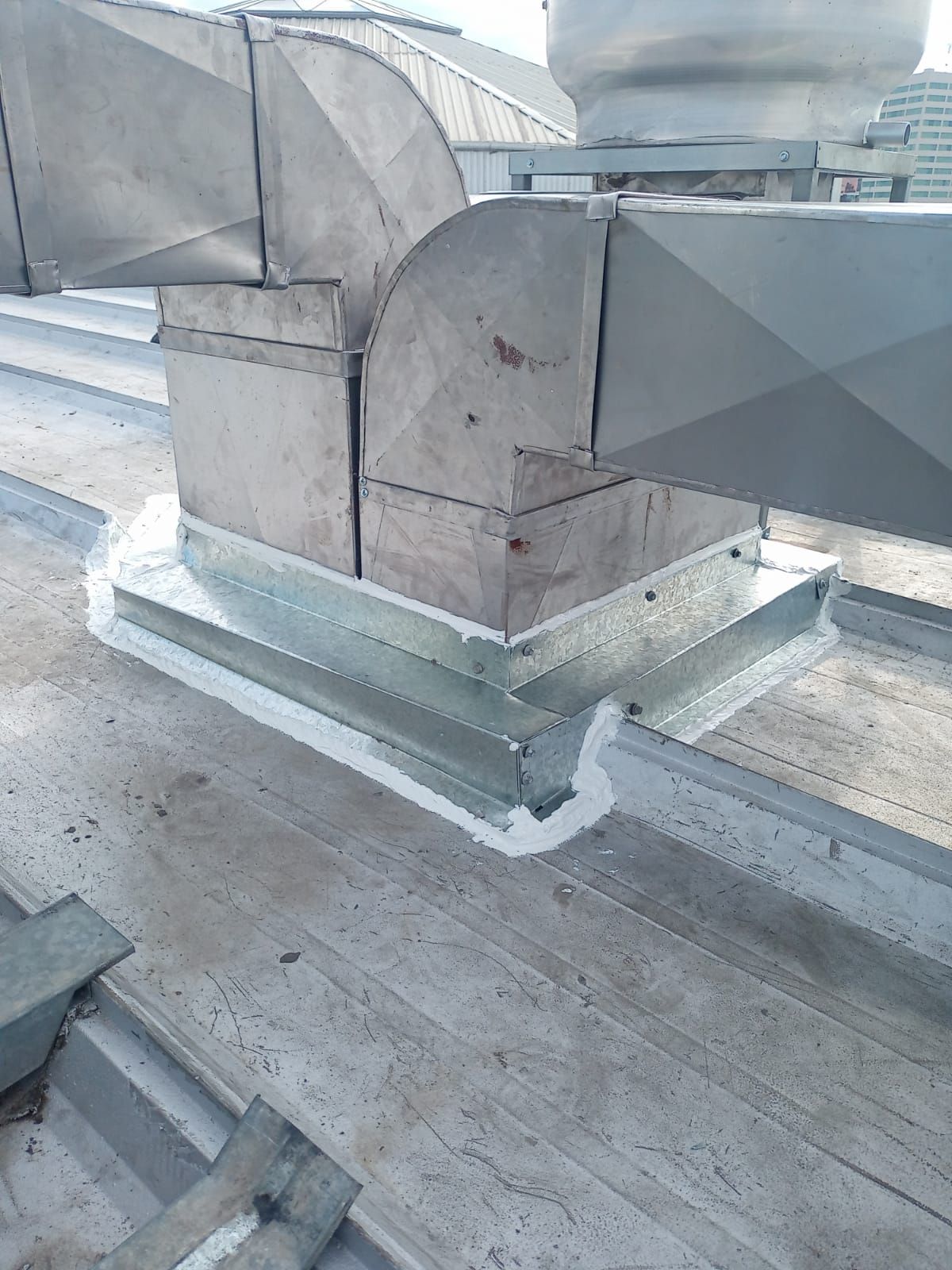 Un remate de canaleta de metal galvanizado en un techo plano industrial con sellador blanco alrededor de la base.