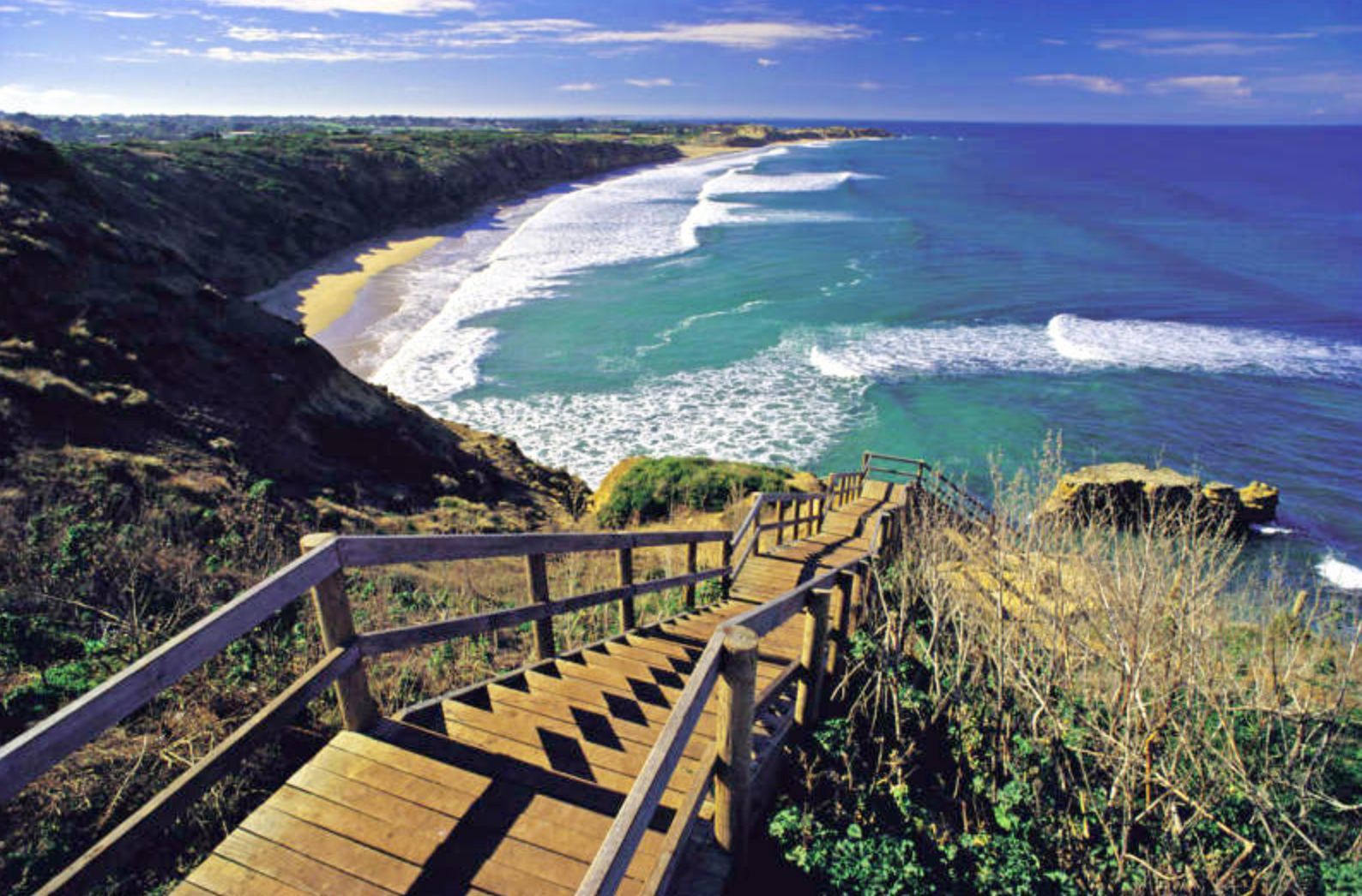 Great Ocean Road scenic coastal landscape with turquoise waters, white sandy beach, green cliffs and wooden boardwalk stairs overlooking iconic Australian tourist destination near Melbourne