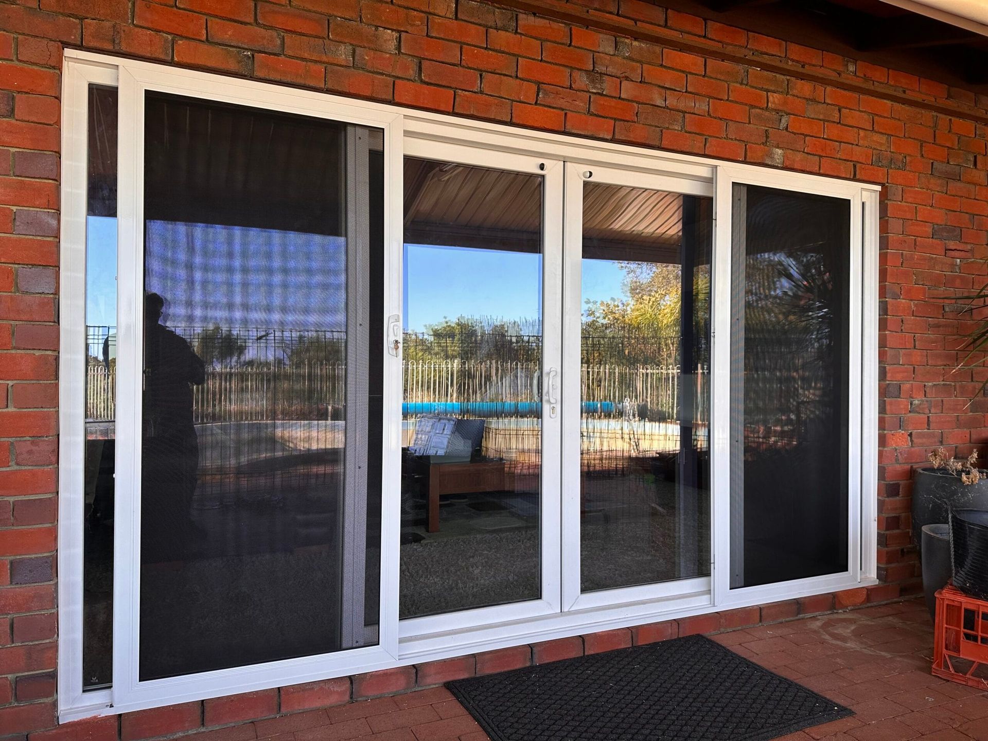 White-framed sliding glass doors with black screens against a brick wall, overlooking a pool.