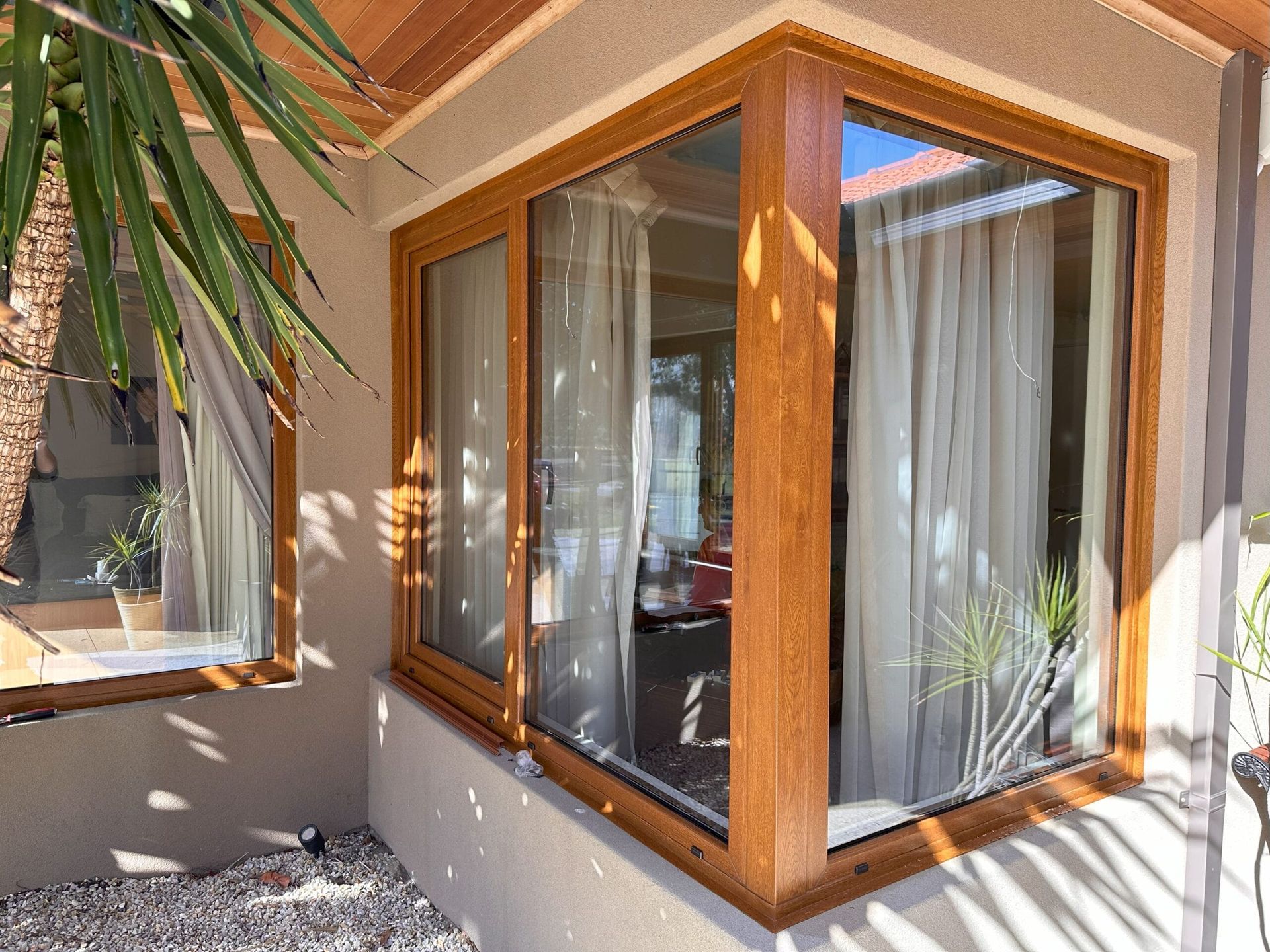 Corner windows with wood frames reflect a sunny interior and exterior foliage.