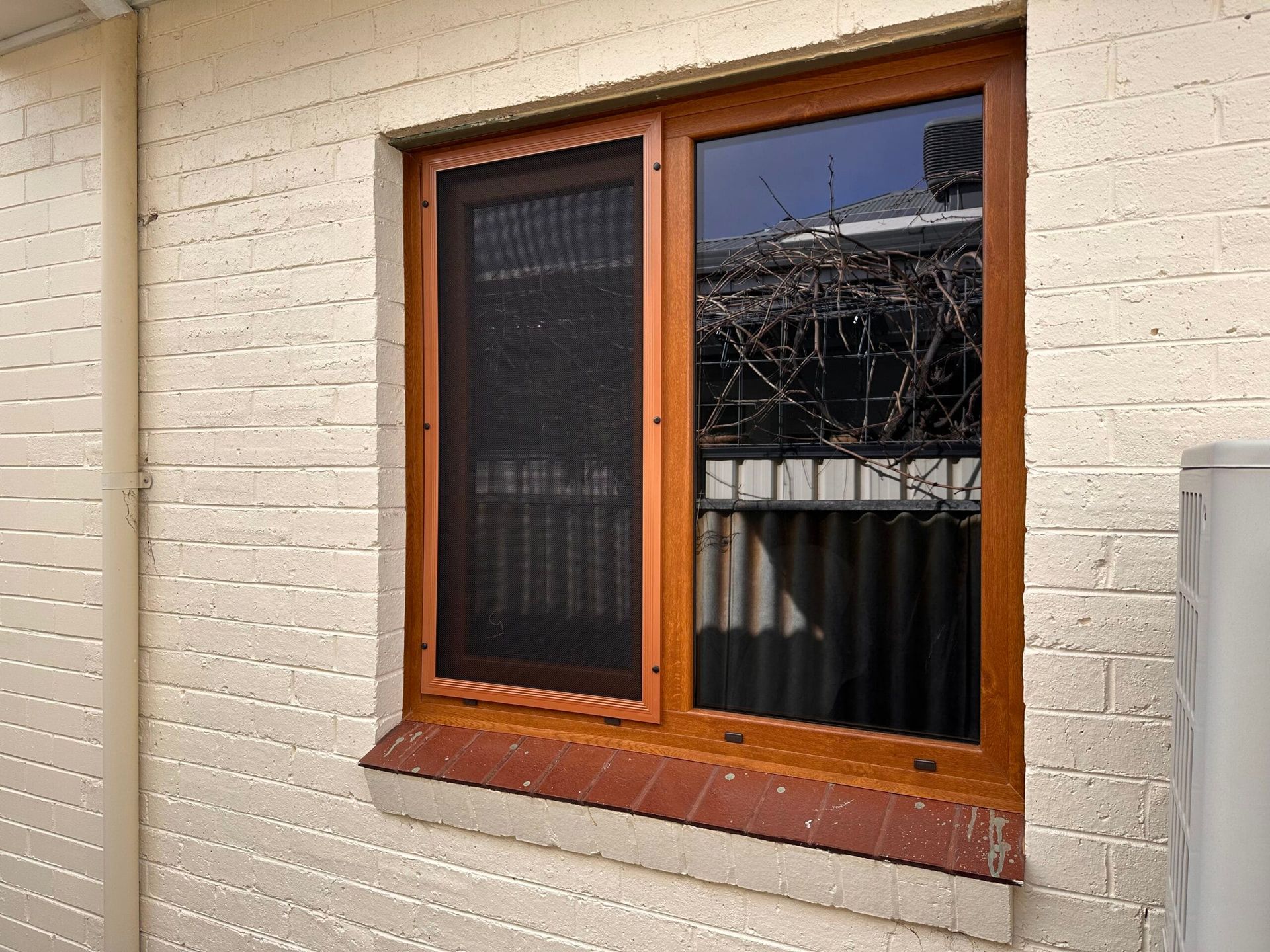 Wooden-framed window with a screen and glass panes, set in a brick wall.