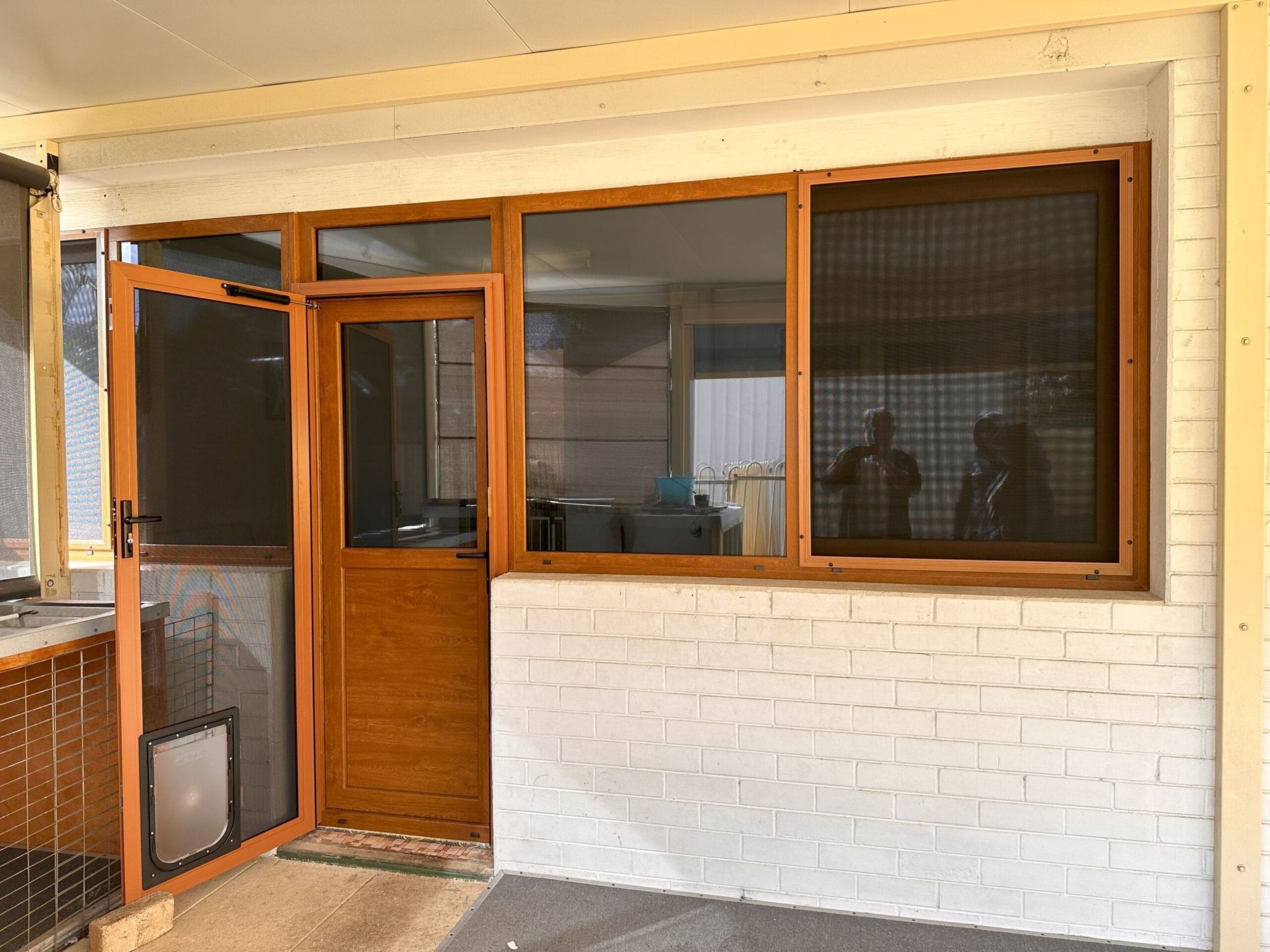 Wooden door and window with screens on a white brick wall, under a covered porch.