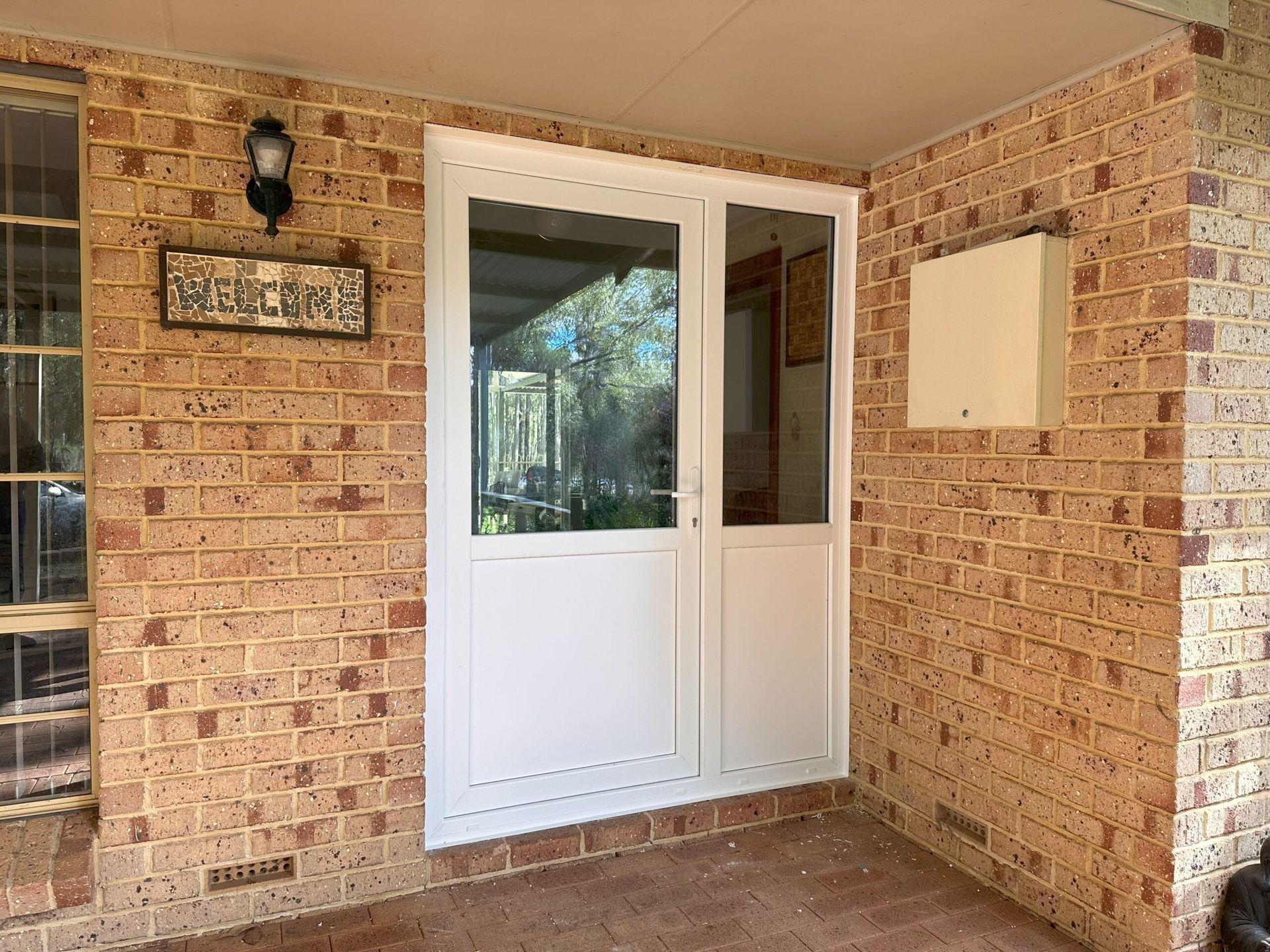 White door with sidelight in brick doorway; porch setting.