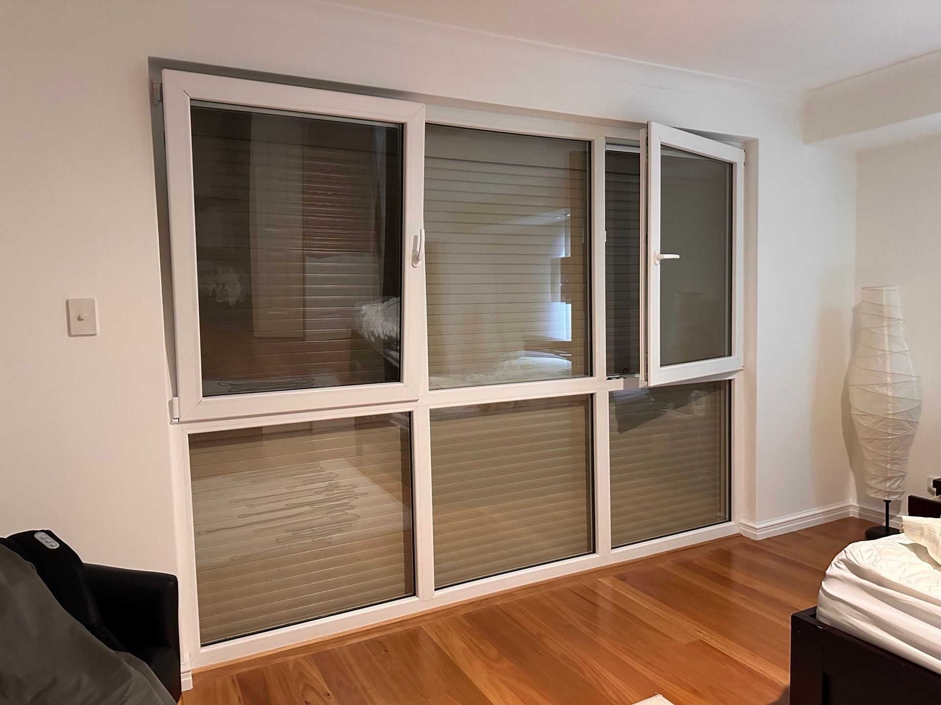 White-framed windows with blinds. One window is open, revealing a view. Wooden floor.