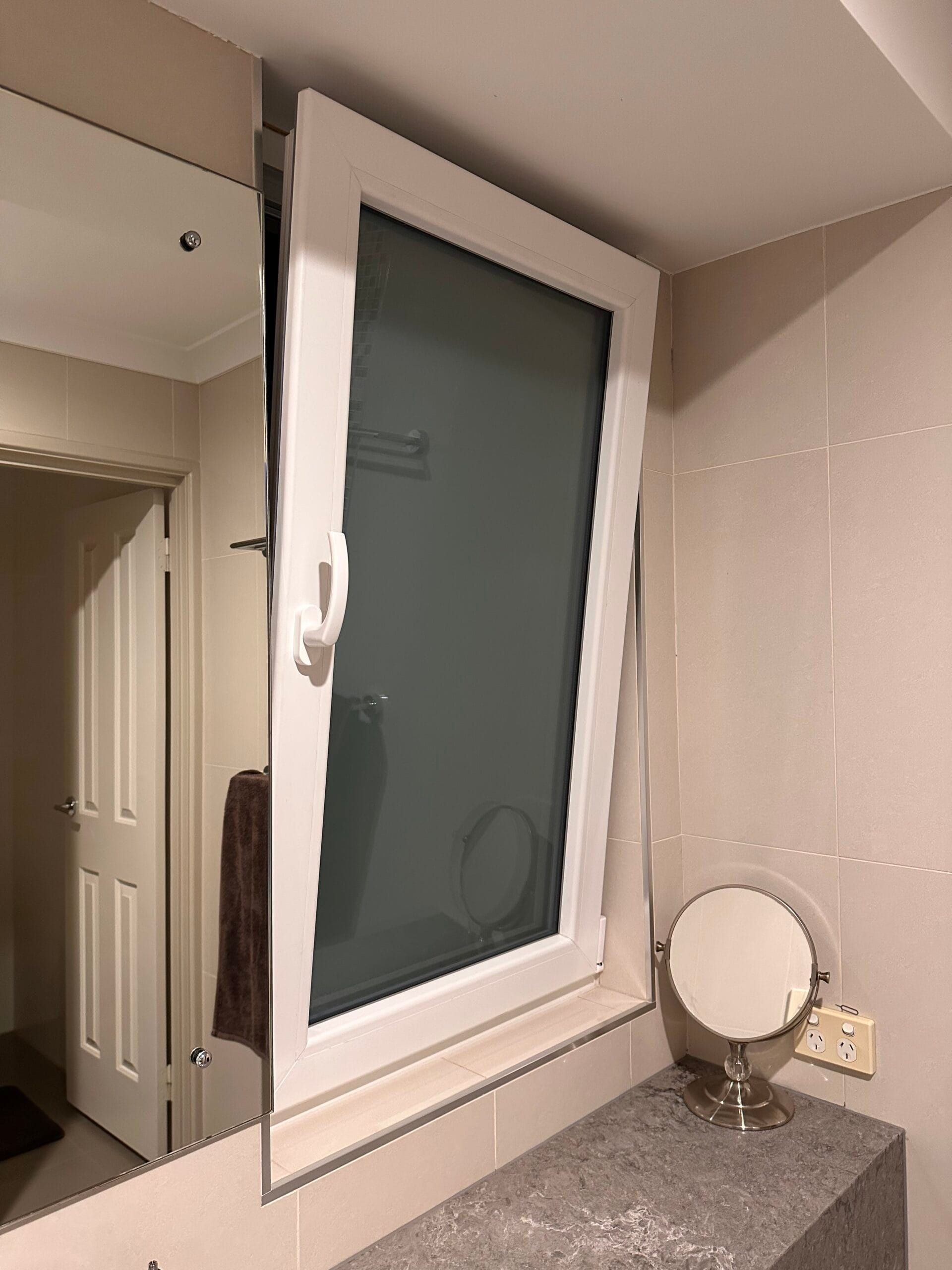 White window in a bathroom over a vanity with a mirror and a small makeup mirror.