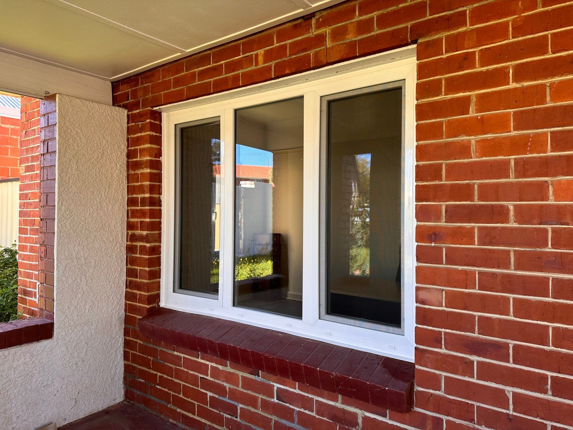 Brick exterior with a white-framed triple window. Window sill and surrounding walls are red brick.