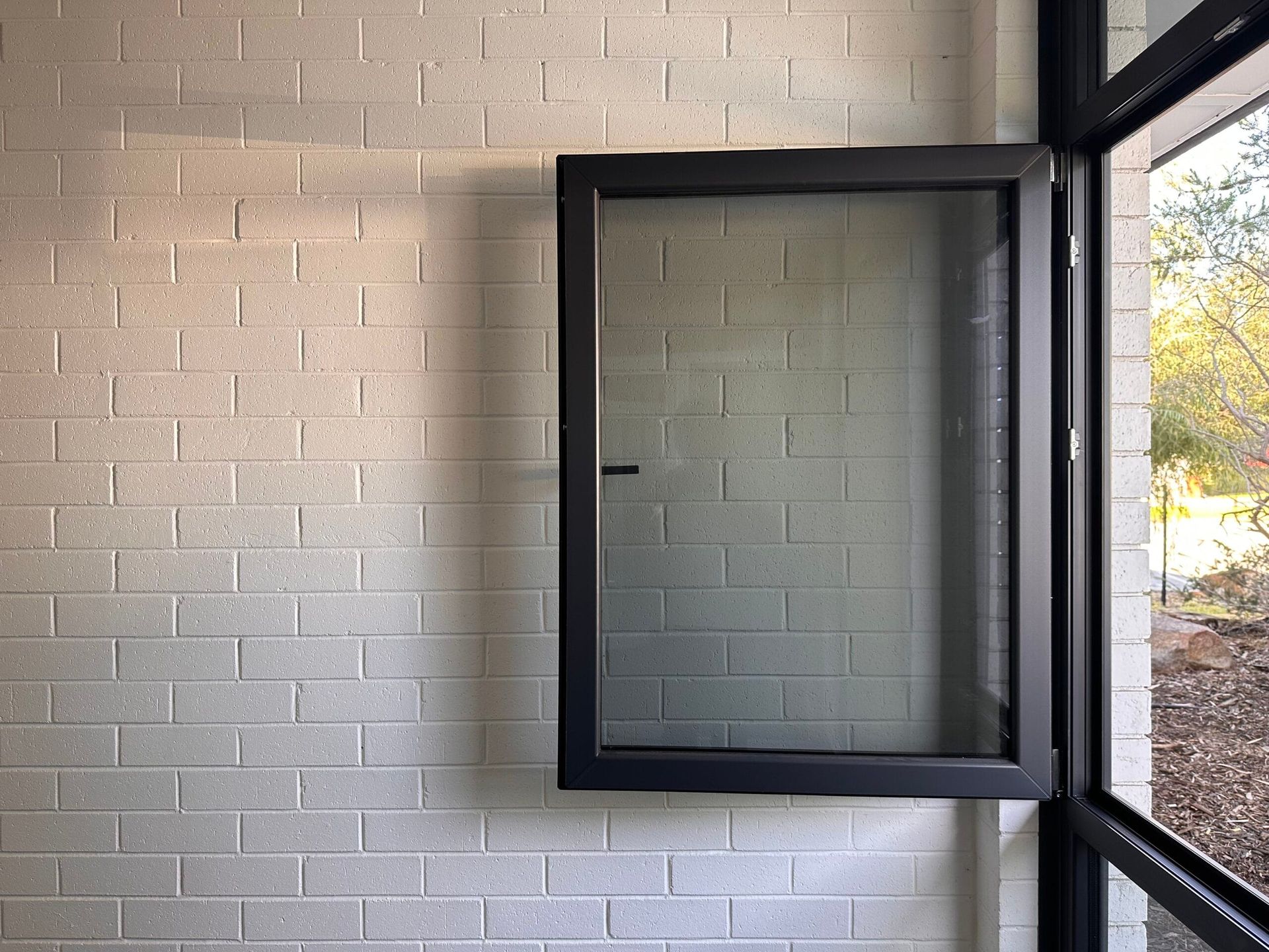 Black-framed window with a screen is open against a white brick wall. View of outside.