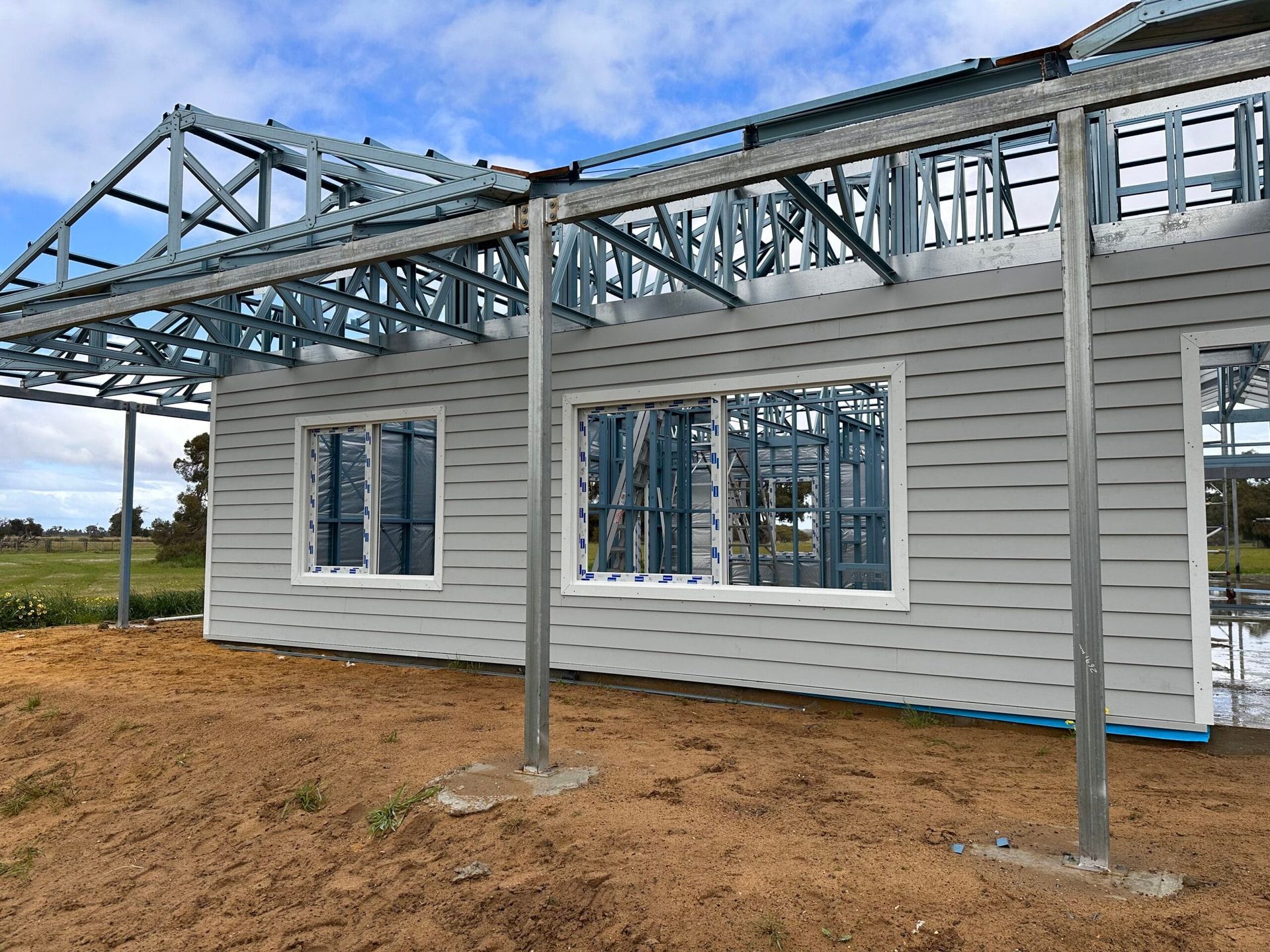 Exterior of a house under construction; gray siding, metal frame, windows, and exposed roof supports.