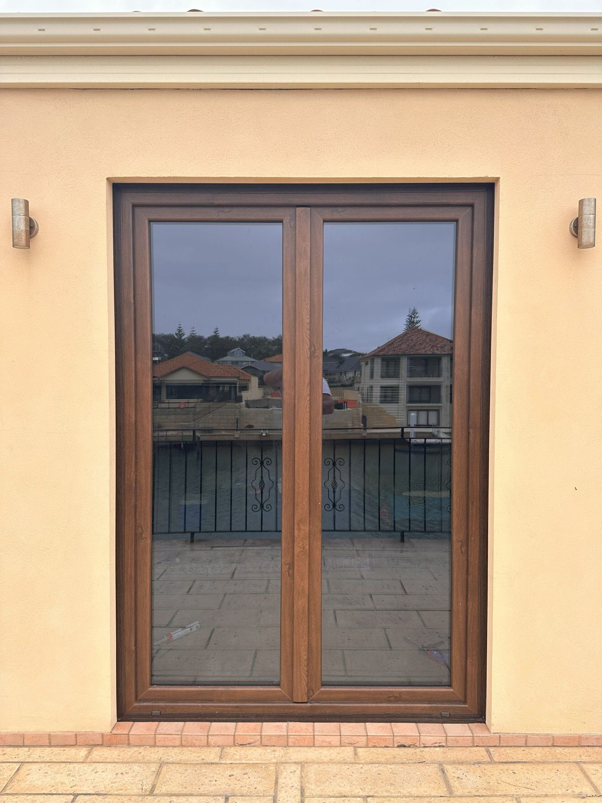 Brown double doors with tinted glass, set in a light beige wall. Rooftop view visible through the glass.