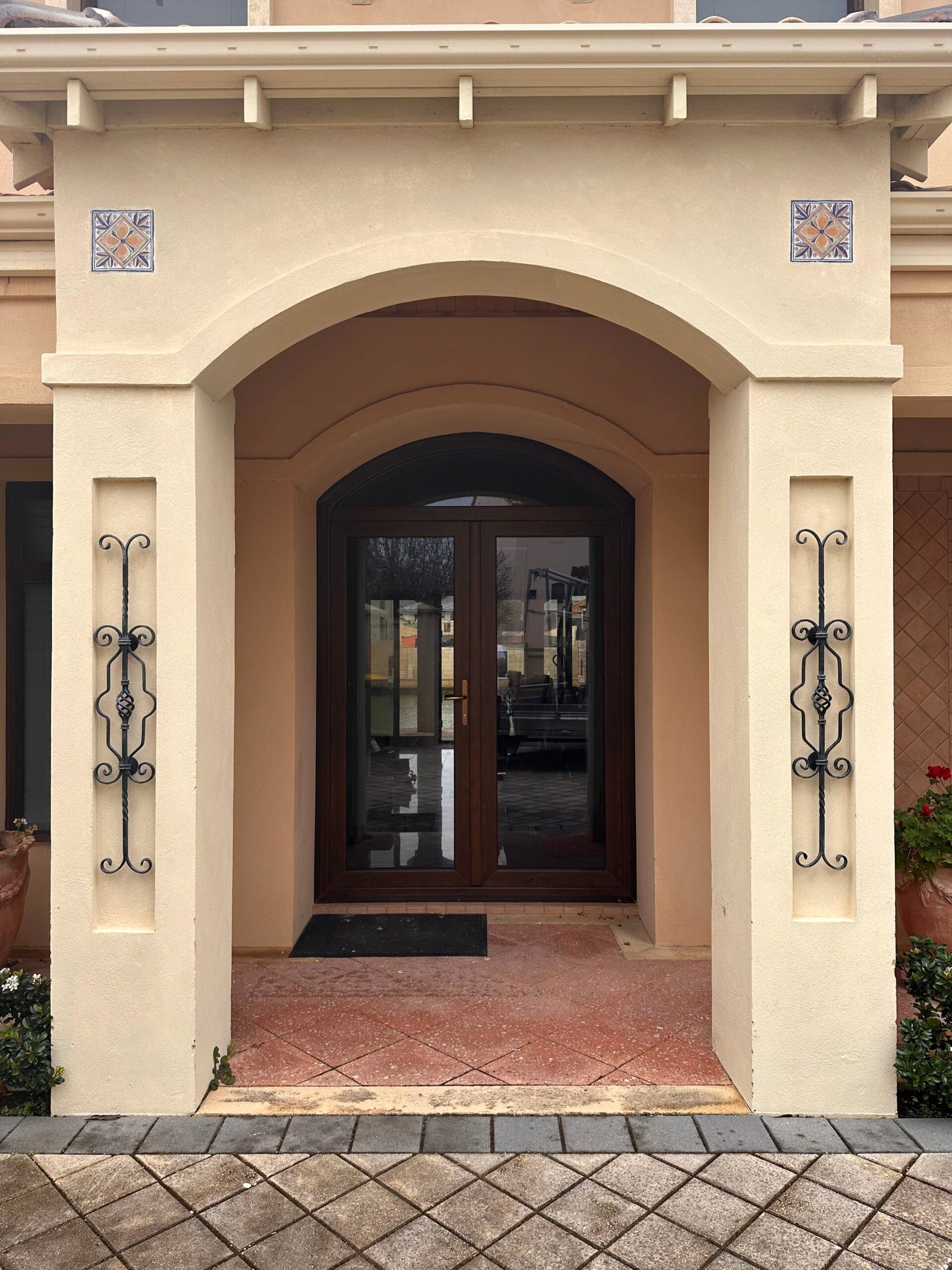 Beige arched doorway with decorative ironwork, dark double doors, and tiled accents.