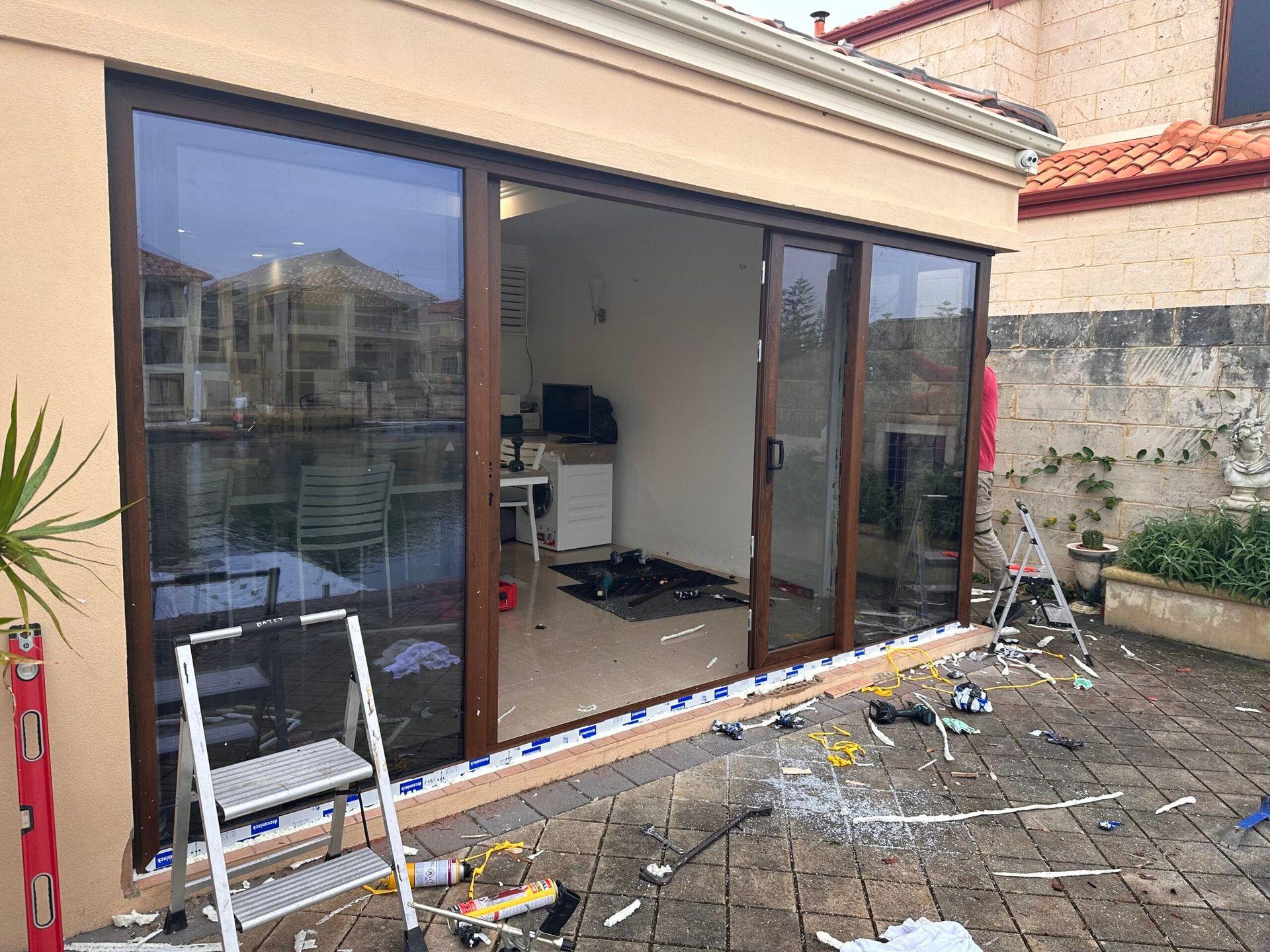Exterior view of brown sliding glass doors during installation, tools and debris visible on the patio.