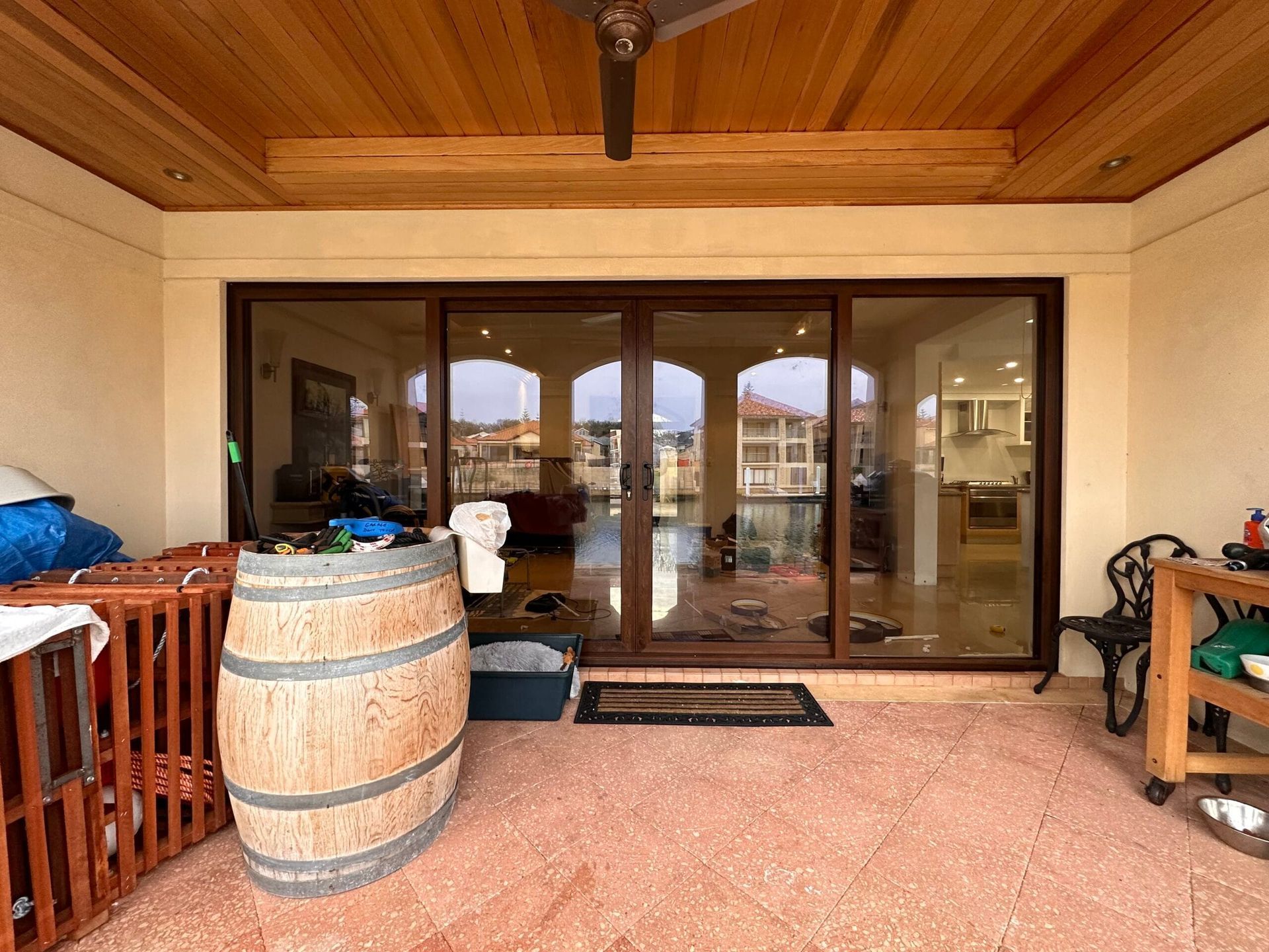 Exterior of a home with sliding glass doors, wooden barrel, and red-tiled patio.