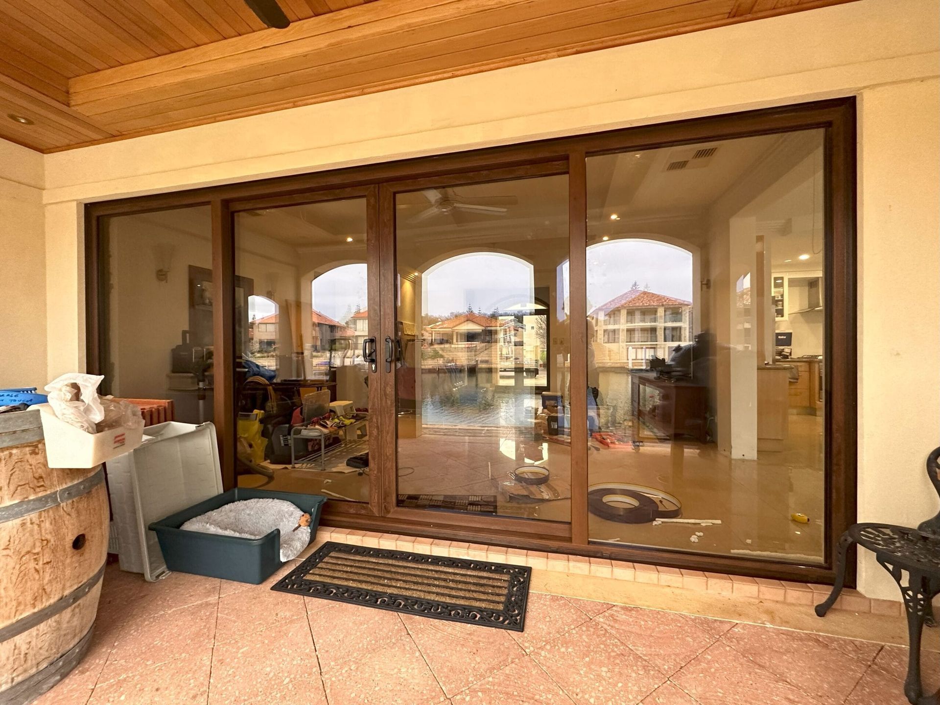 Sliding glass doors open onto a patio with a barrel, dog bed, and view of a canal and house interior.