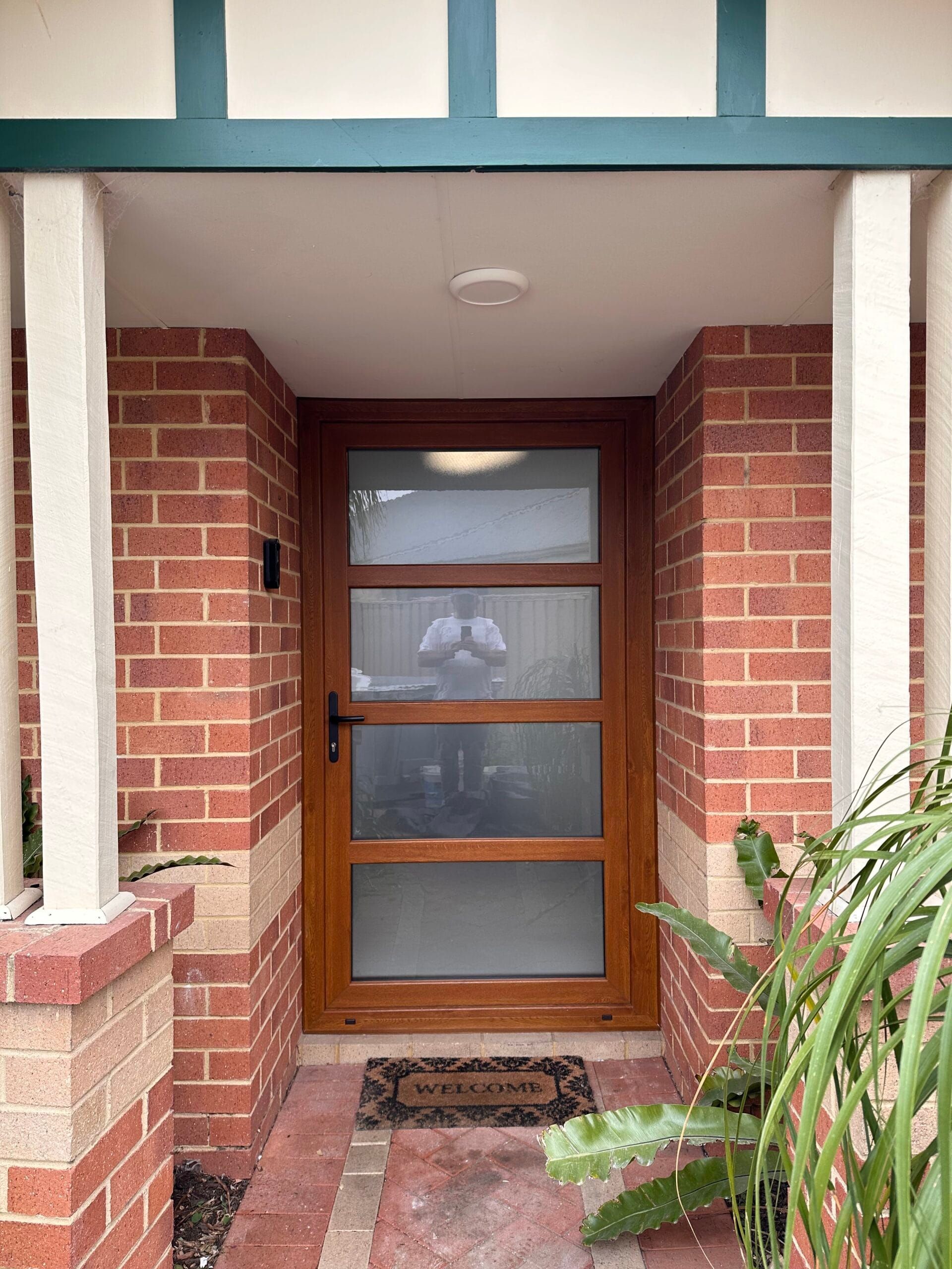 Wooden door with glass panels framed by brick, under a covered entry.