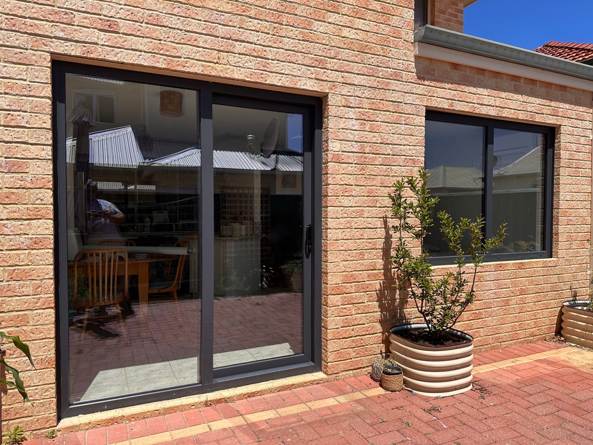 Sliding glass door and window with black frames on brick building exterior. Potted plant on brick patio.