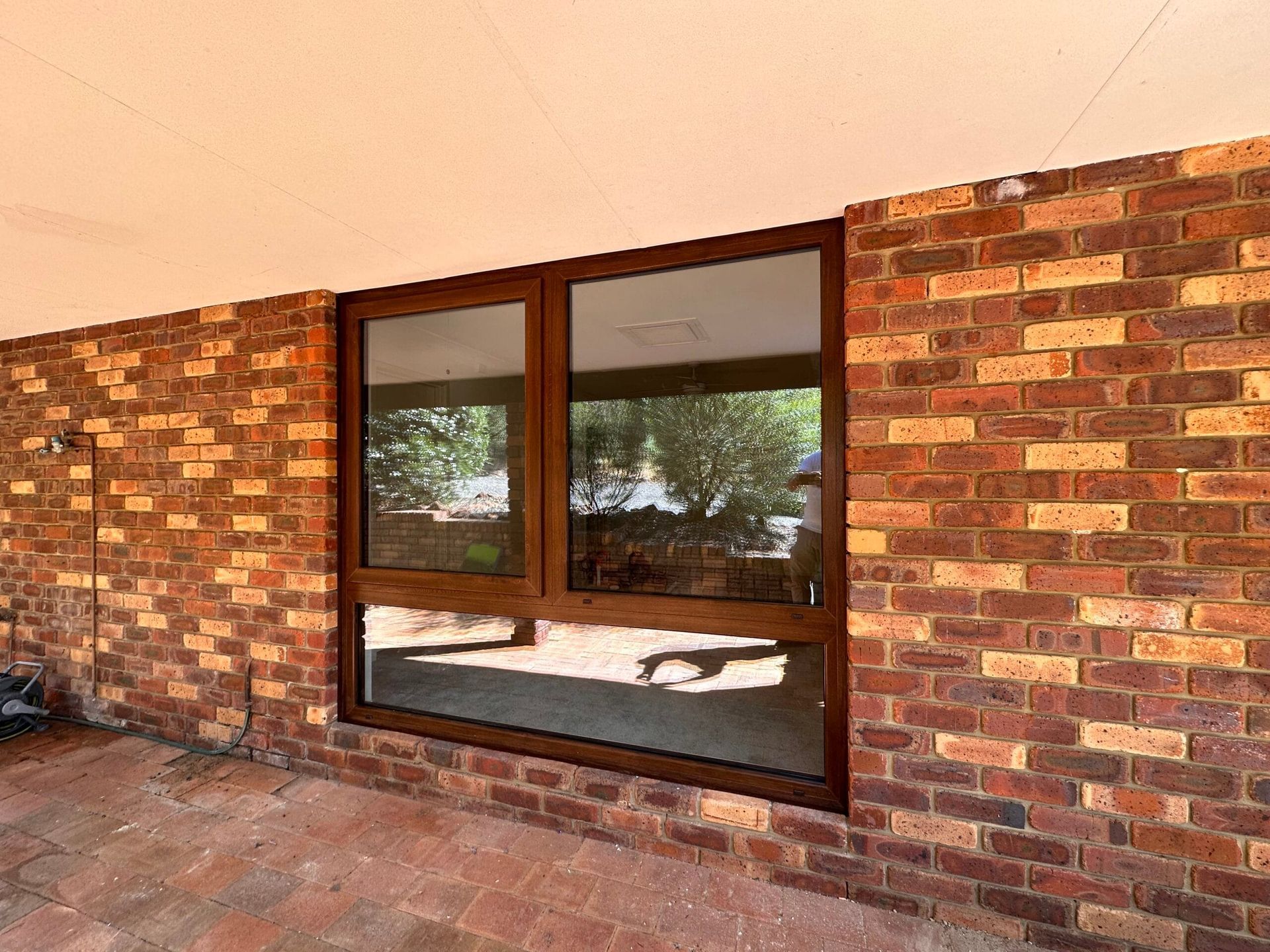 Brown window in brick wall, reflecting trees and sky.