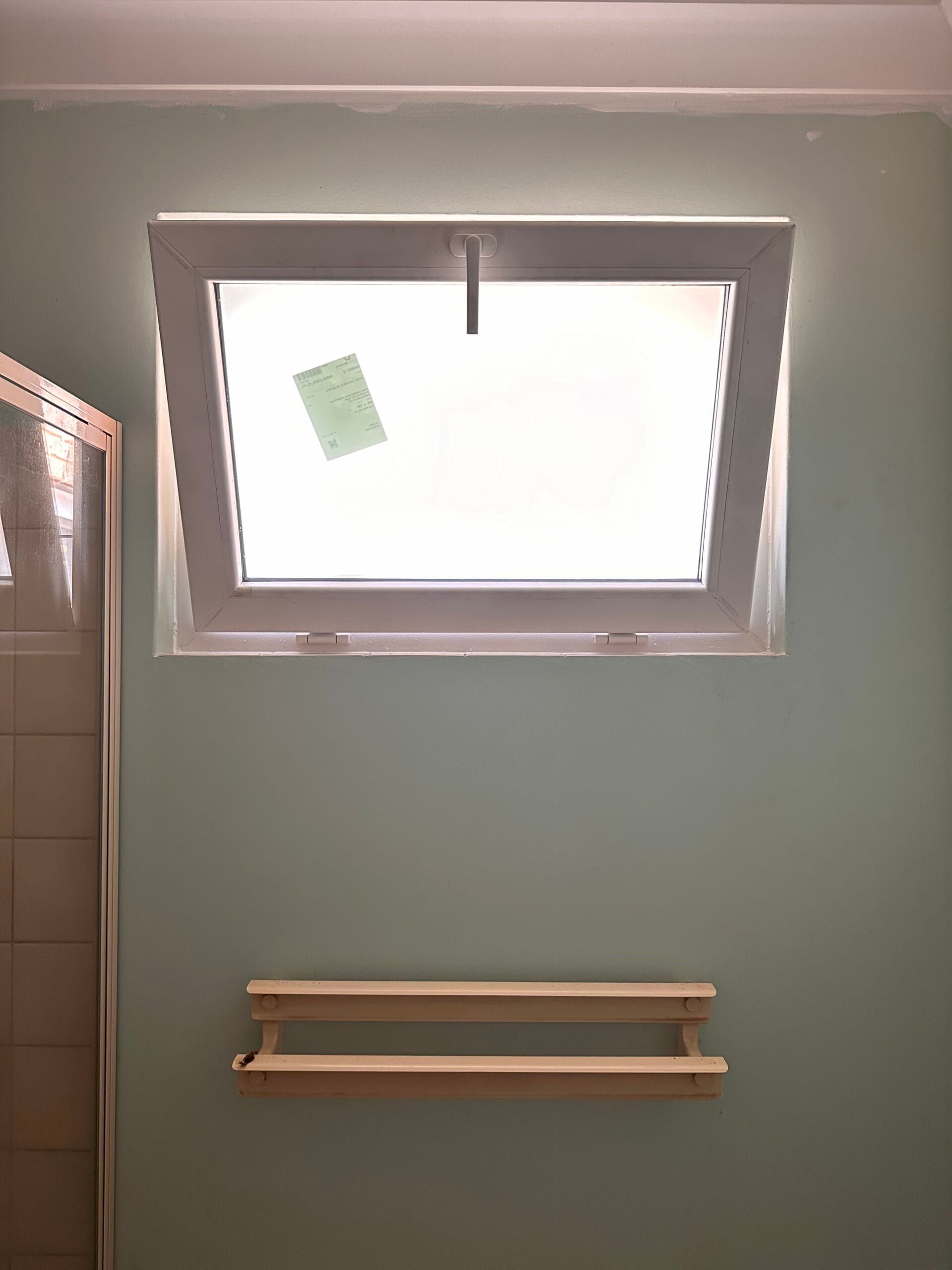Bathroom with open white-framed window. Light green wall. Wooden shelf below the window.