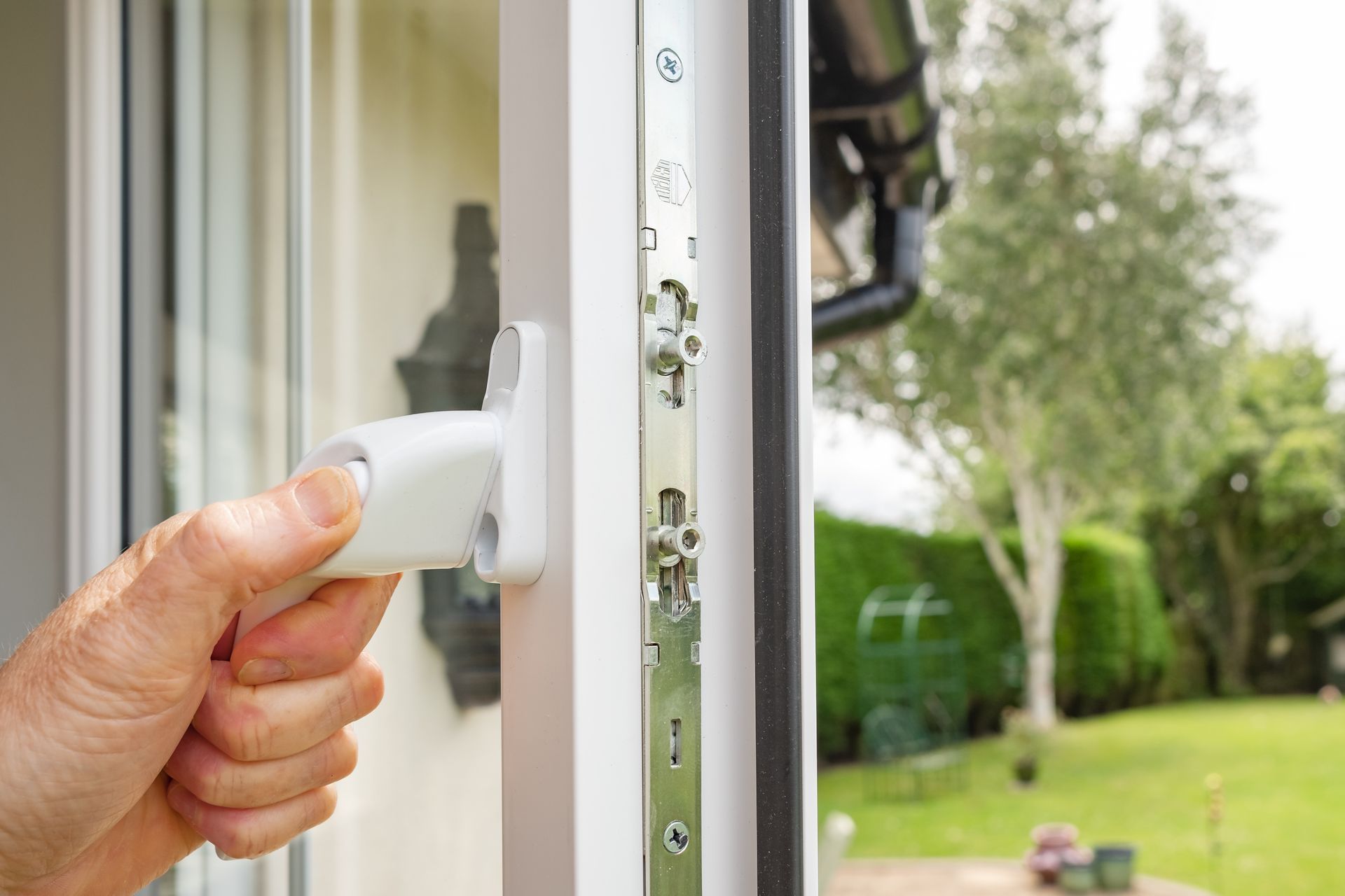 A person opening a double-glazed door adjacent to a large garden.