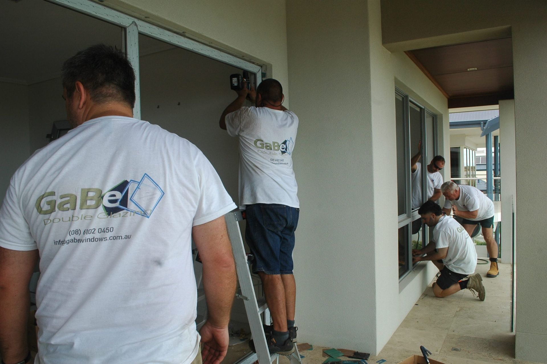 Workers in white shirts install windows on a building exterior.