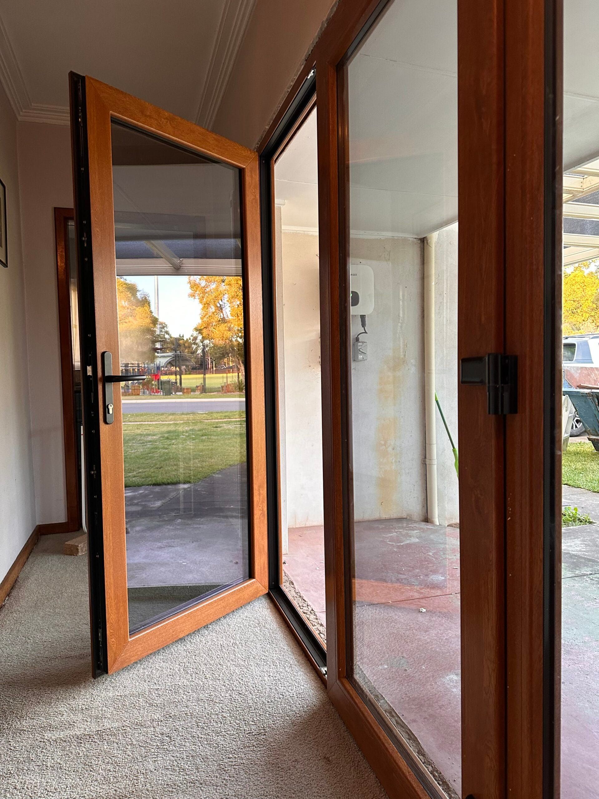 Open wooden-framed glass doors revealing a green yard and driveway.