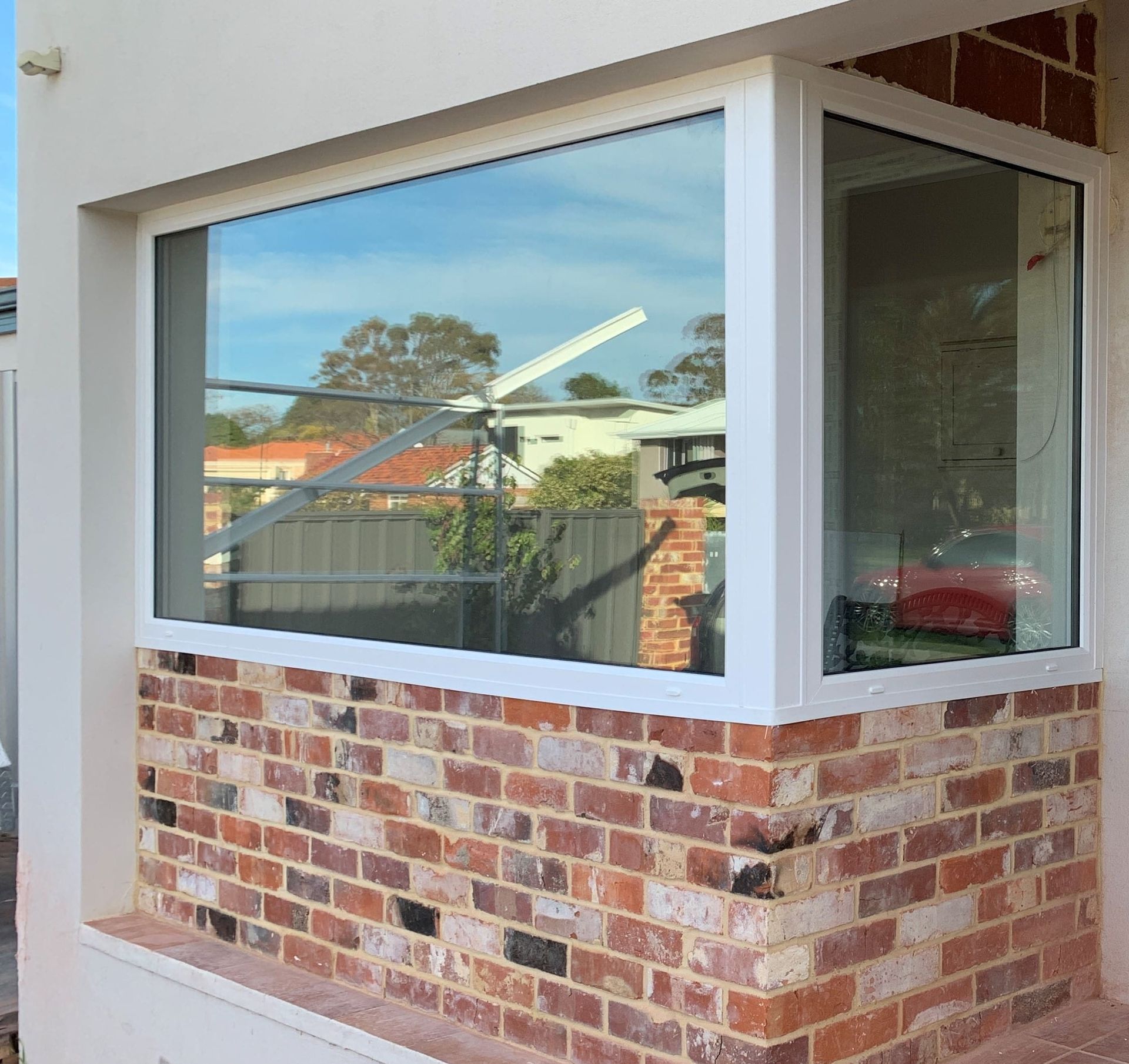 Brick wall with a large, white-framed window. The window reflects the sky and trees.
