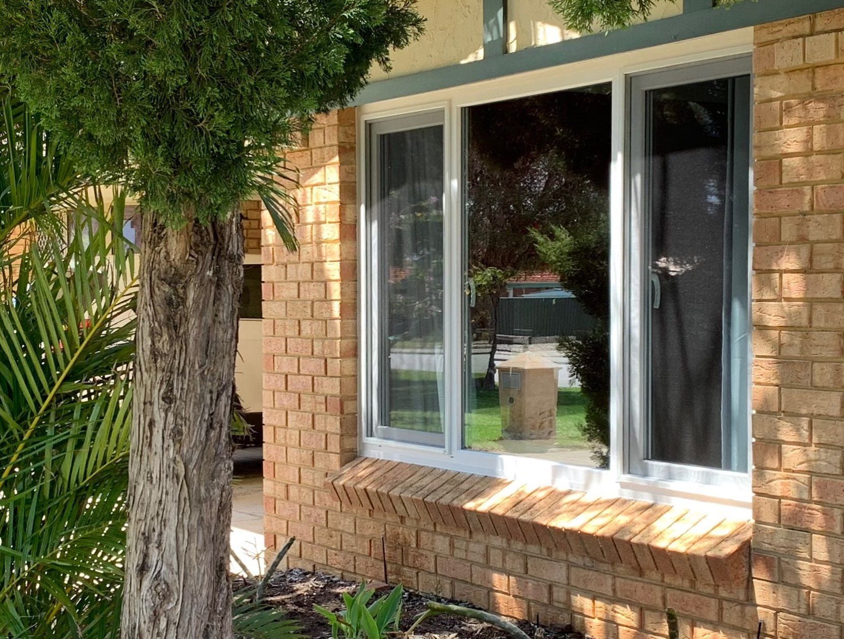 Brick building with three pane windows. A tree partially obscures the view.