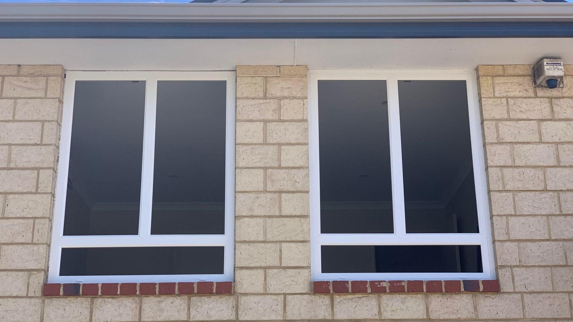 Two white-framed windows on a light brick wall, with a small brown brick ledge.