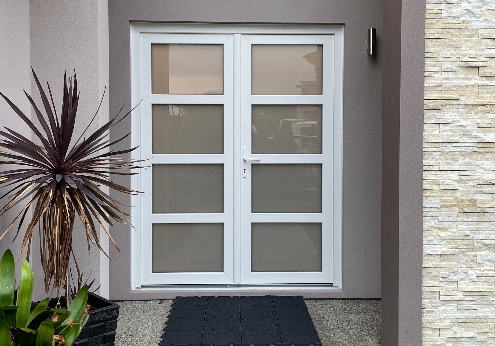 White double doors with glass panels and a black doormat.