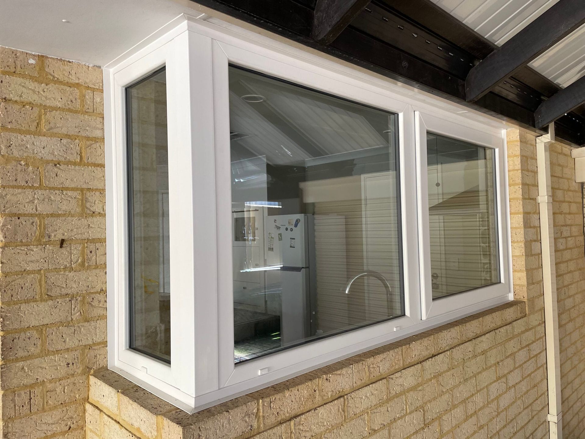 White framed bay window on a brick exterior. Reflecting a kitchen and a partially visible roof.