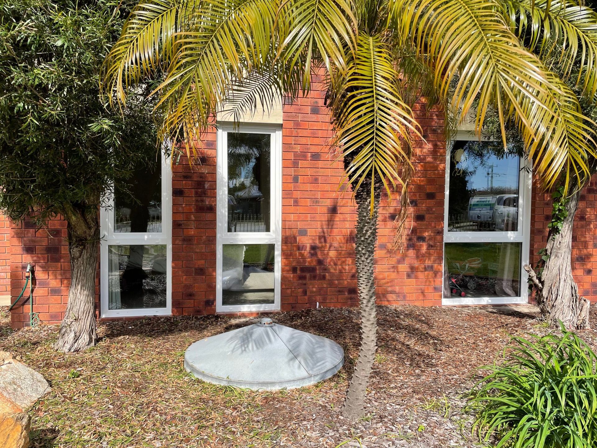 Red brick building with three vertical windows, palm tree, and landscaping.