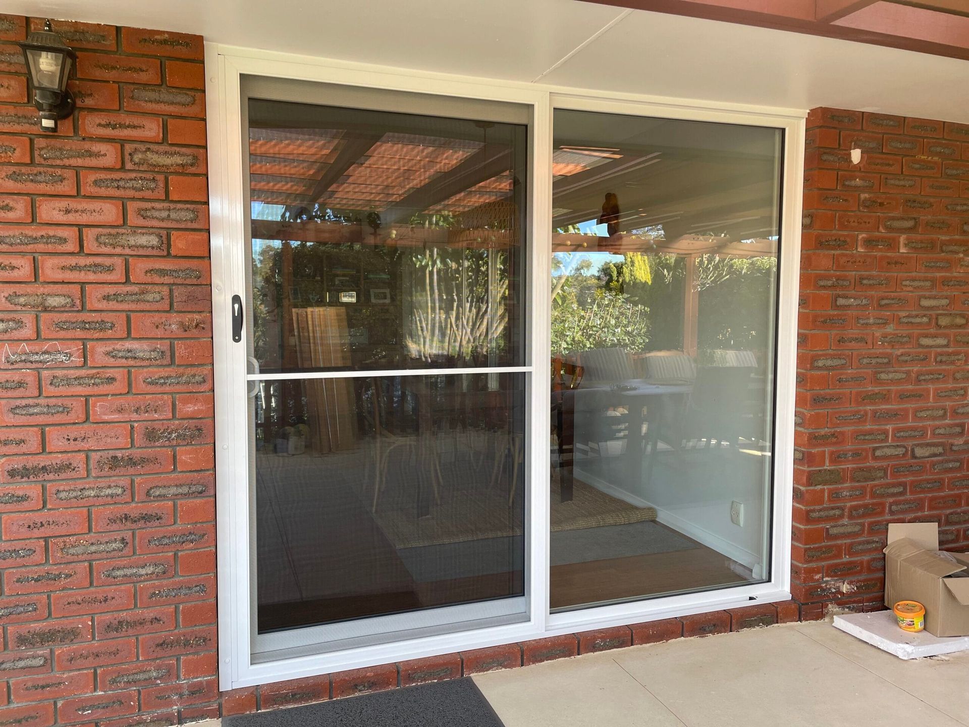 Sliding glass doors with a screen door set in a brick wall. Sunlight reflects in the glass.