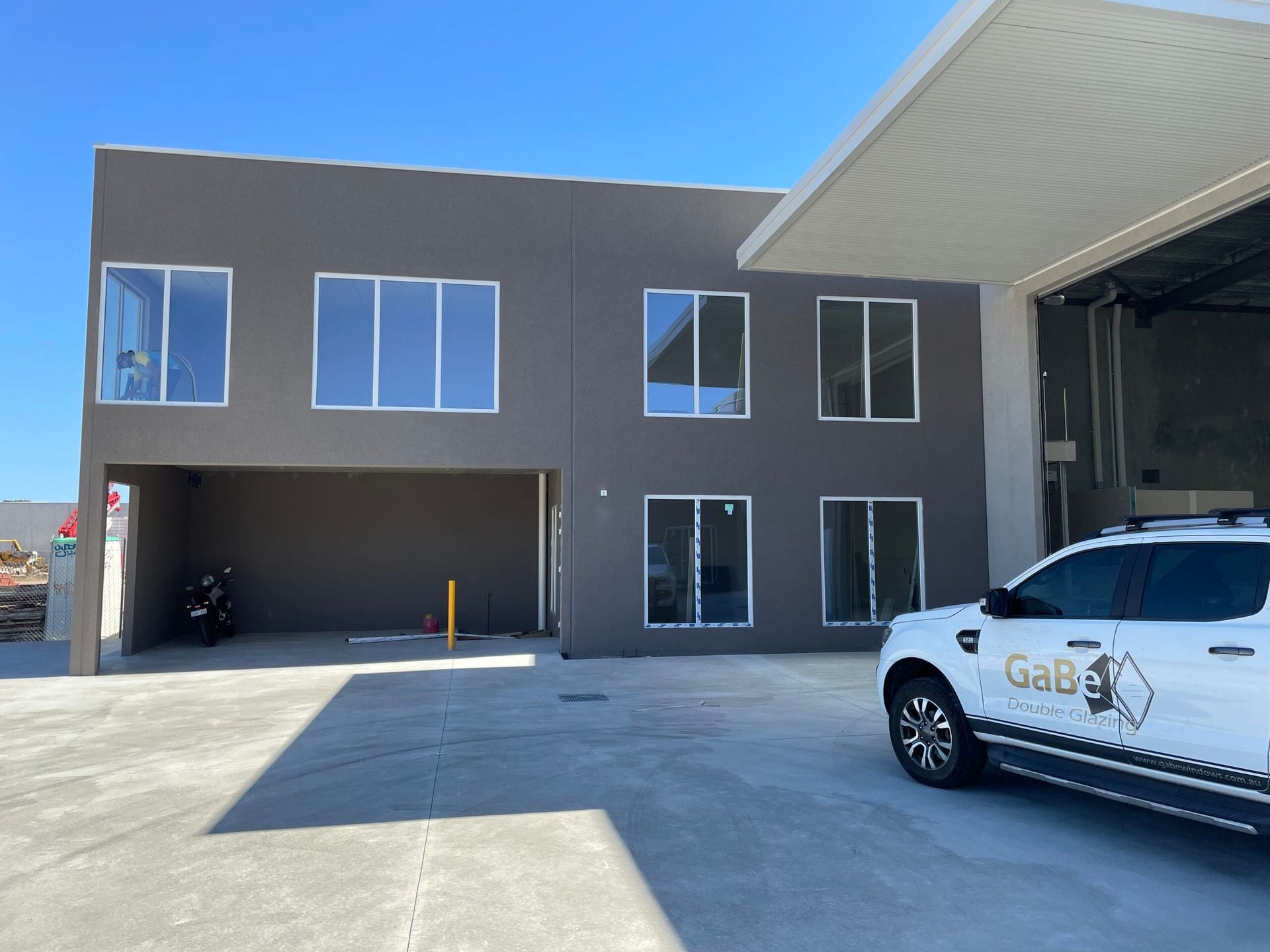 Two-story grey building with multiple windows; a white vehicle with