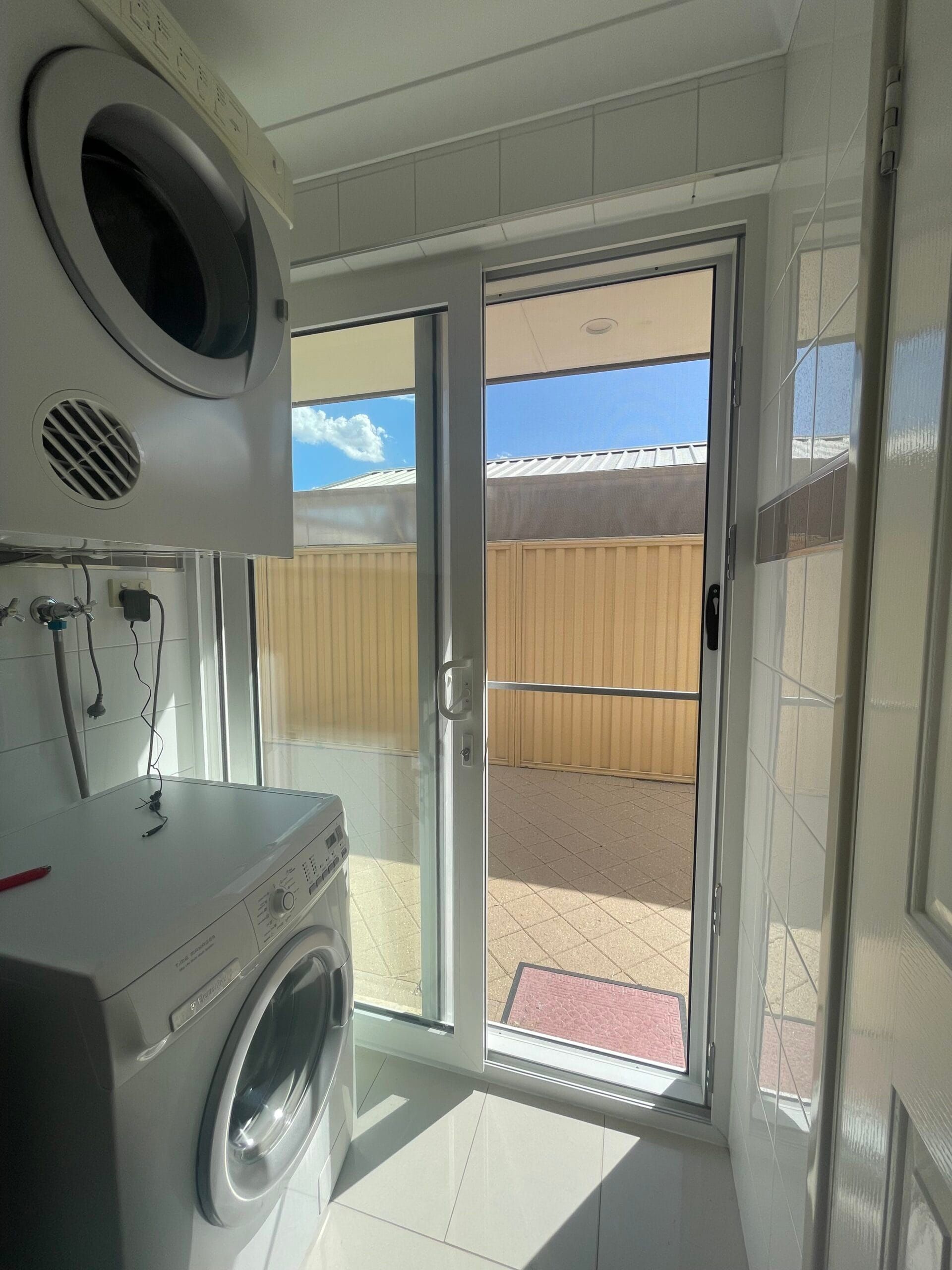 Laundry room with white appliances, door to outside, and view of a sunny yard.