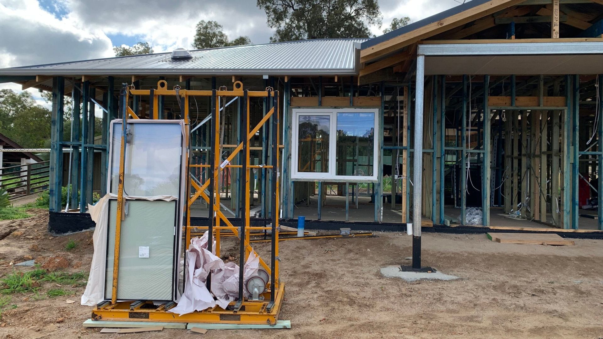 House frame under construction with a window and a lifting machine outside.