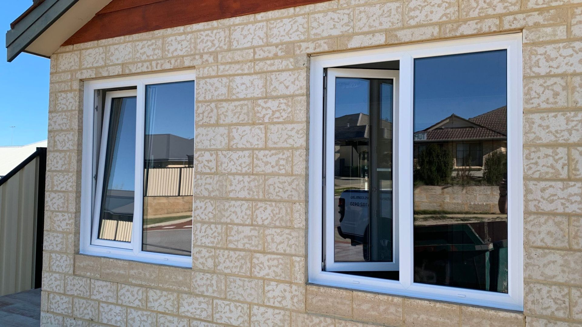 Two white-framed windows on a brick building; one window partially open.