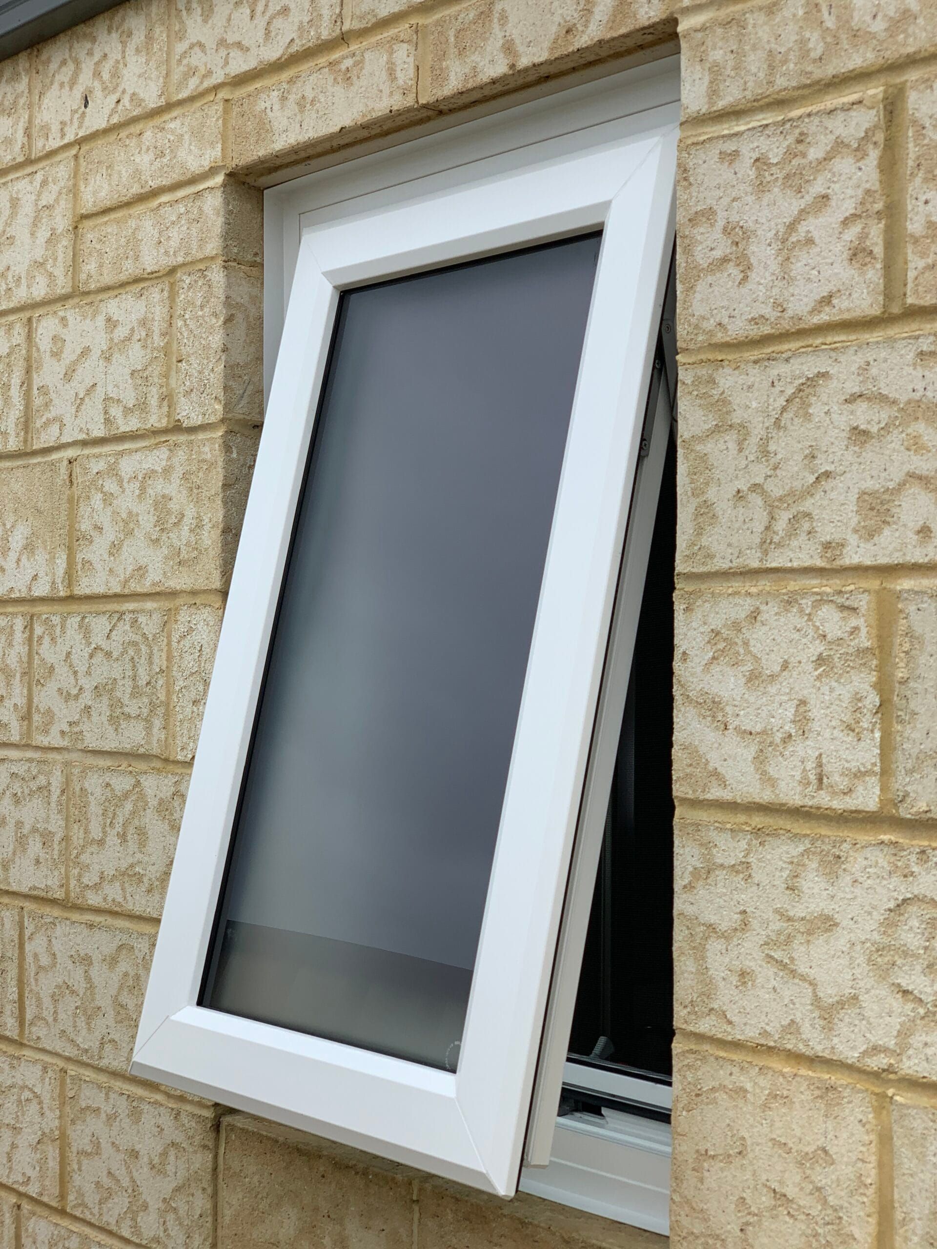White-framed window tilted open on a light beige brick wall.