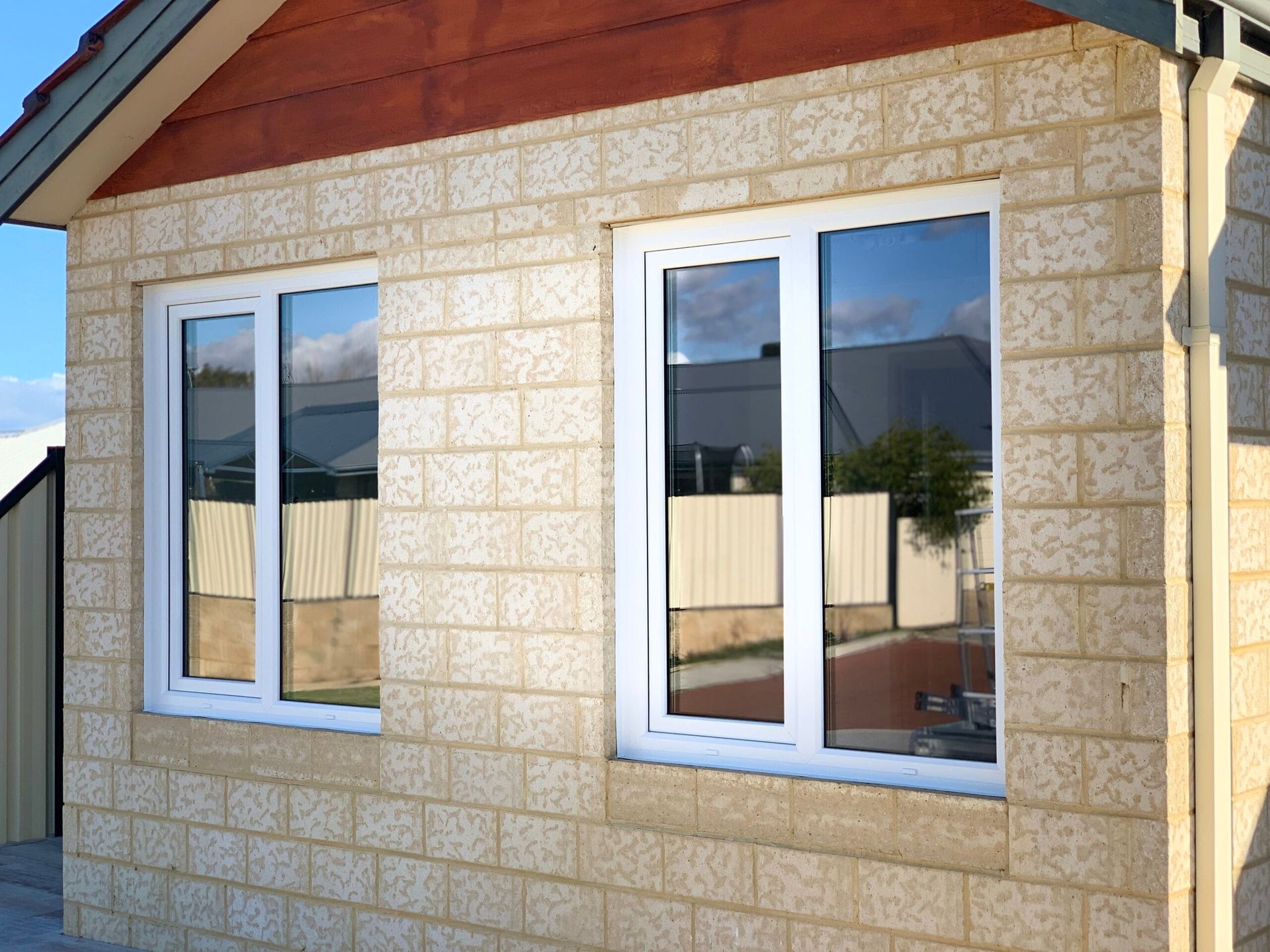 Two white-framed windows on a beige brick building, reflecting the sky and surrounding buildings.