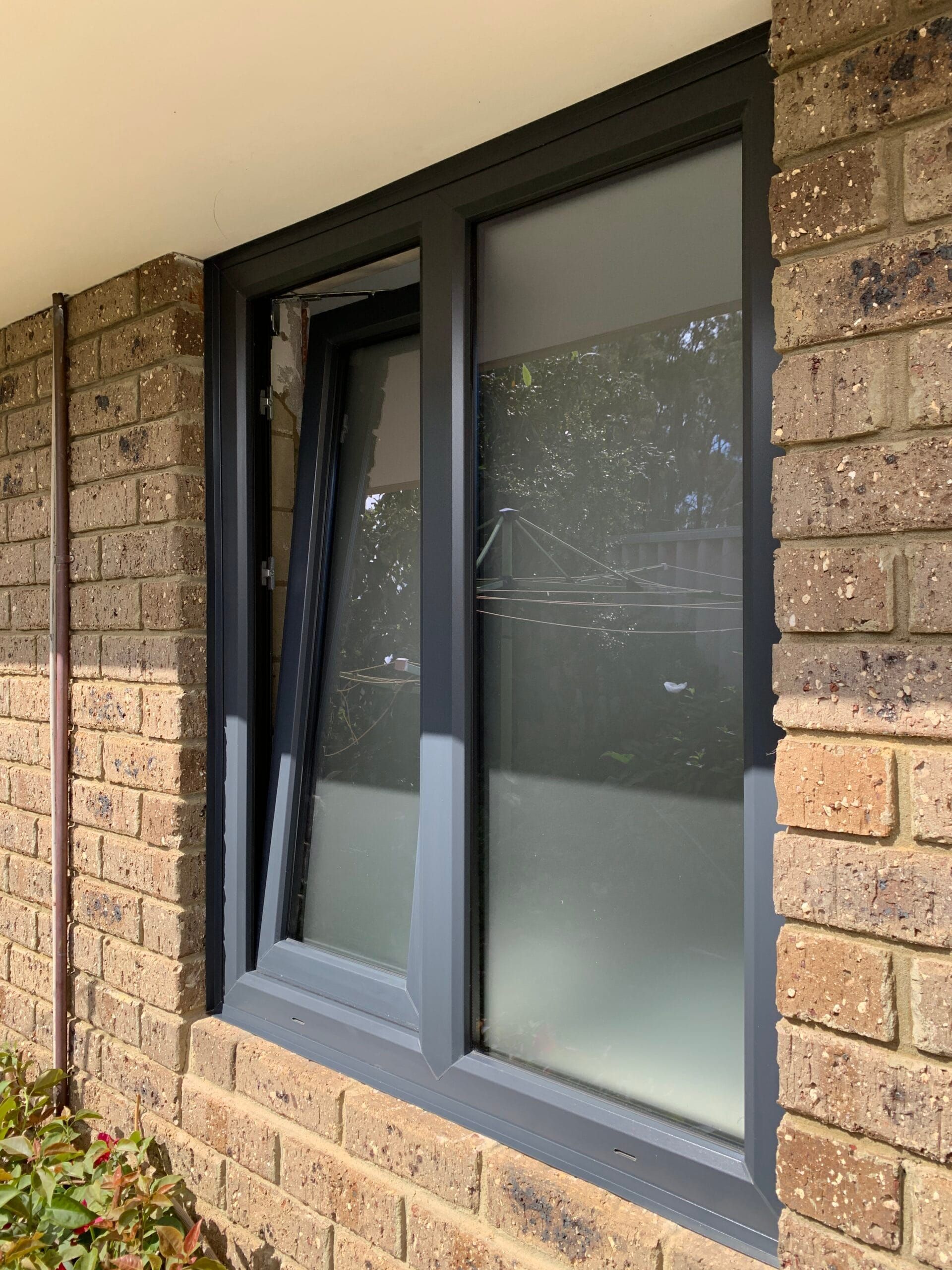 Open gray window in brick wall, one panel tilted open.