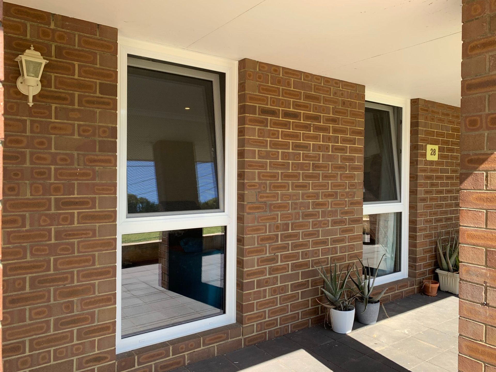 Exterior view of a brick building with two white-framed windows, porch, and potted plants.