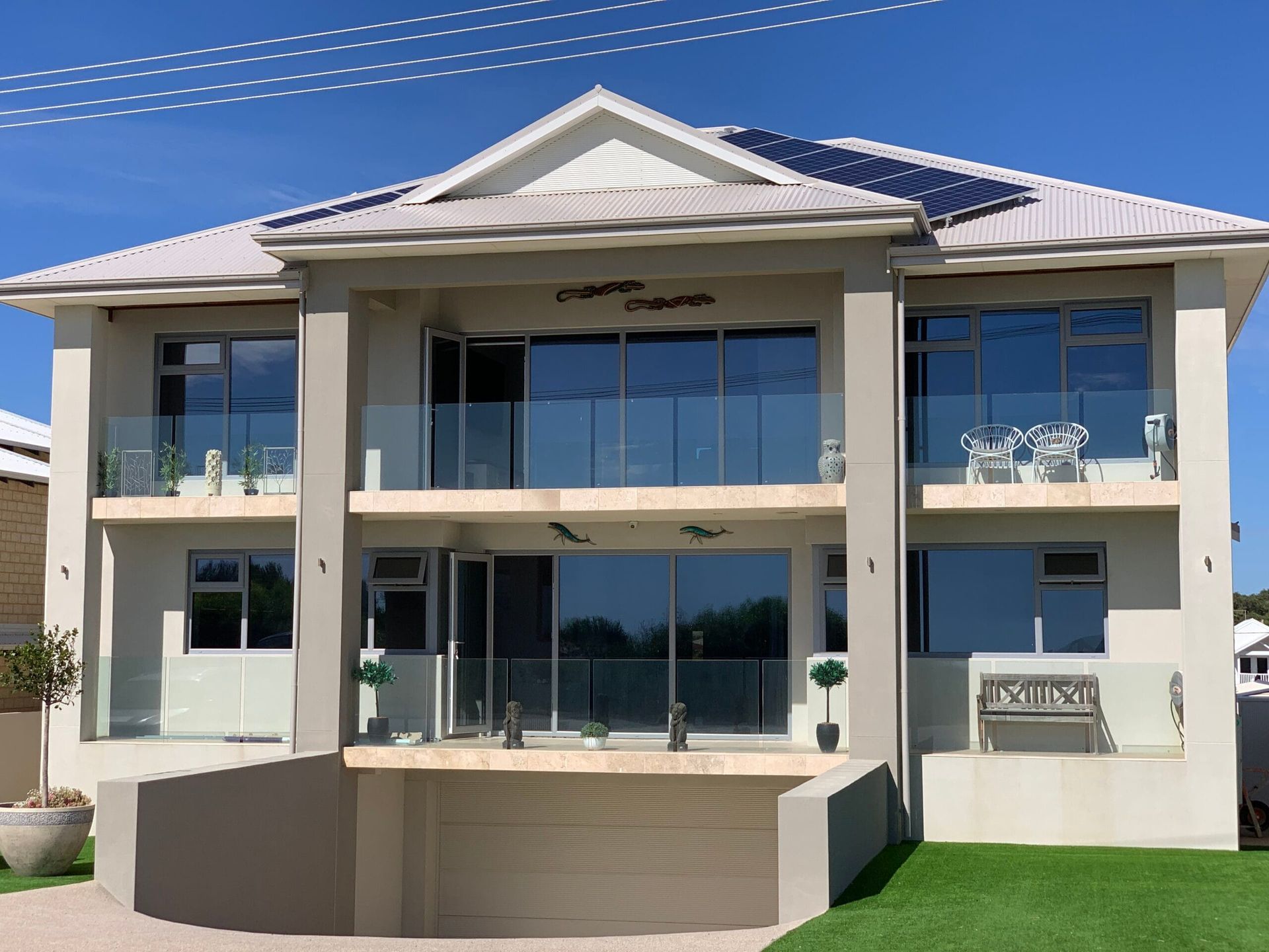 Two-story modern home with balconies, glass railings, solar panels, and a garage on a sunny day.