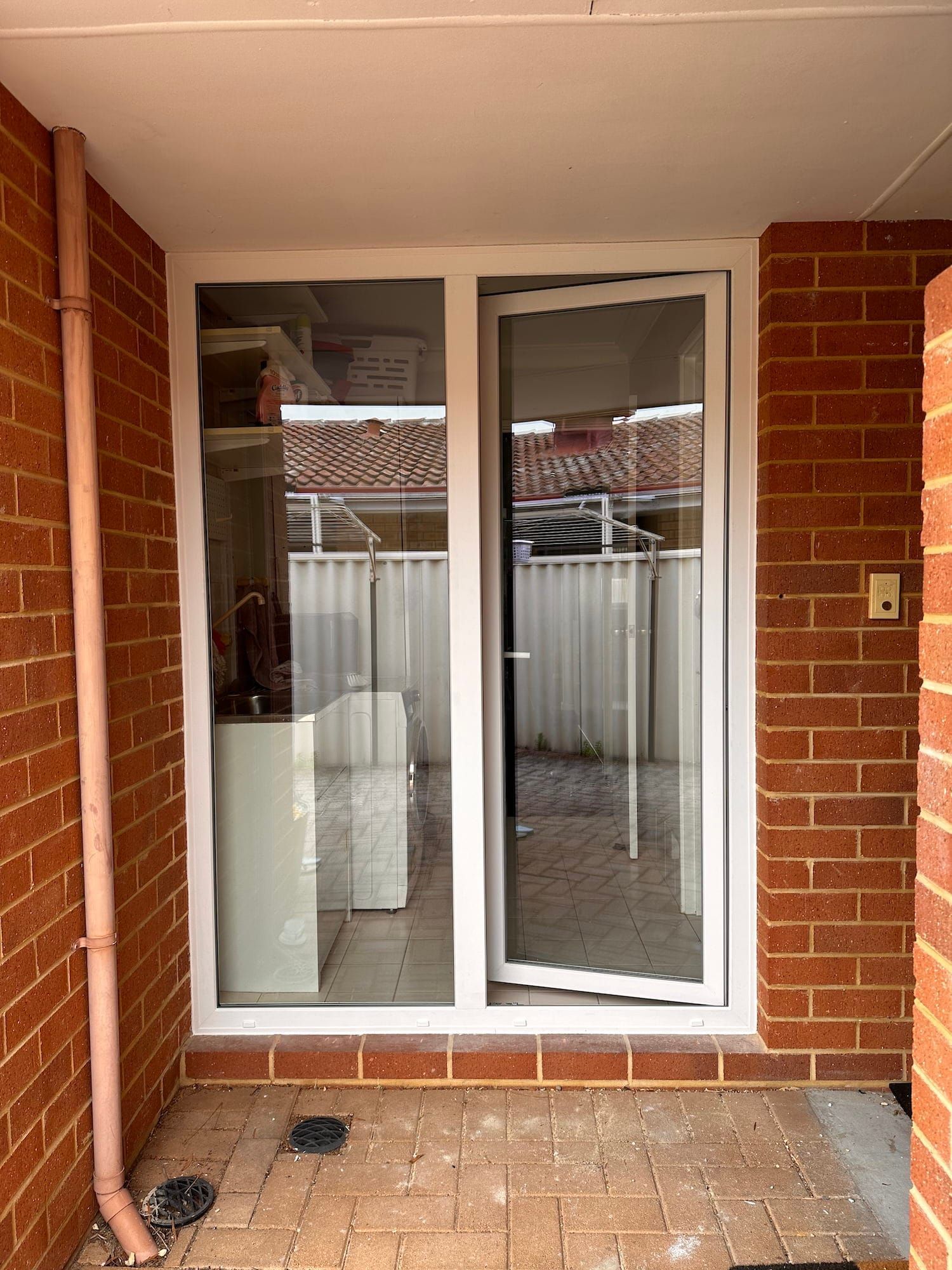 White-framed glass sliding door, one side open, on a brick patio. Red brick walls and a fence are visible through the door.