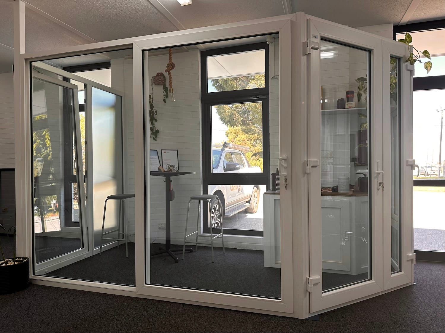 White-framed glass room with a door open to the left. Interior features chairs and a table.