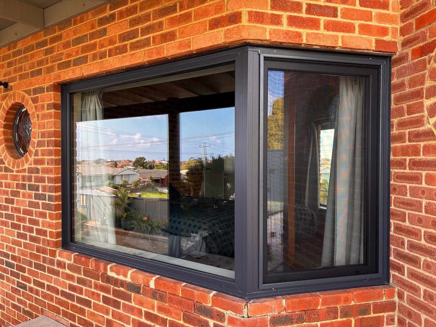 Corner bay window with black trim set in a brick wall, reflecting the outside view.