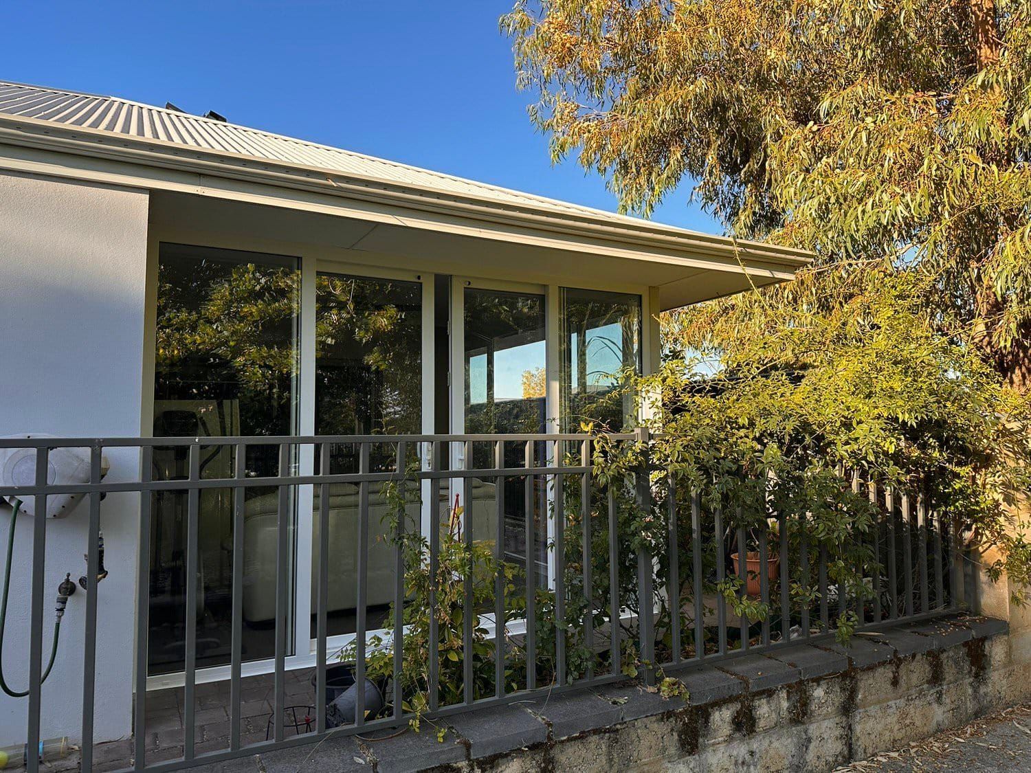 House with large windows, covered by a white roof, and a black wrought-iron fence. Sunny day.
