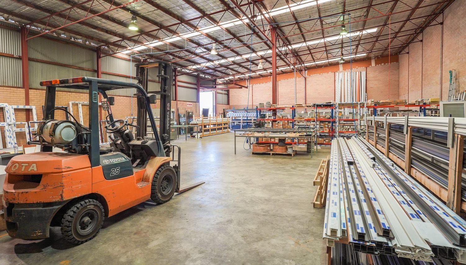 Orange forklift in a warehouse with shelving, products, and a concrete floor.