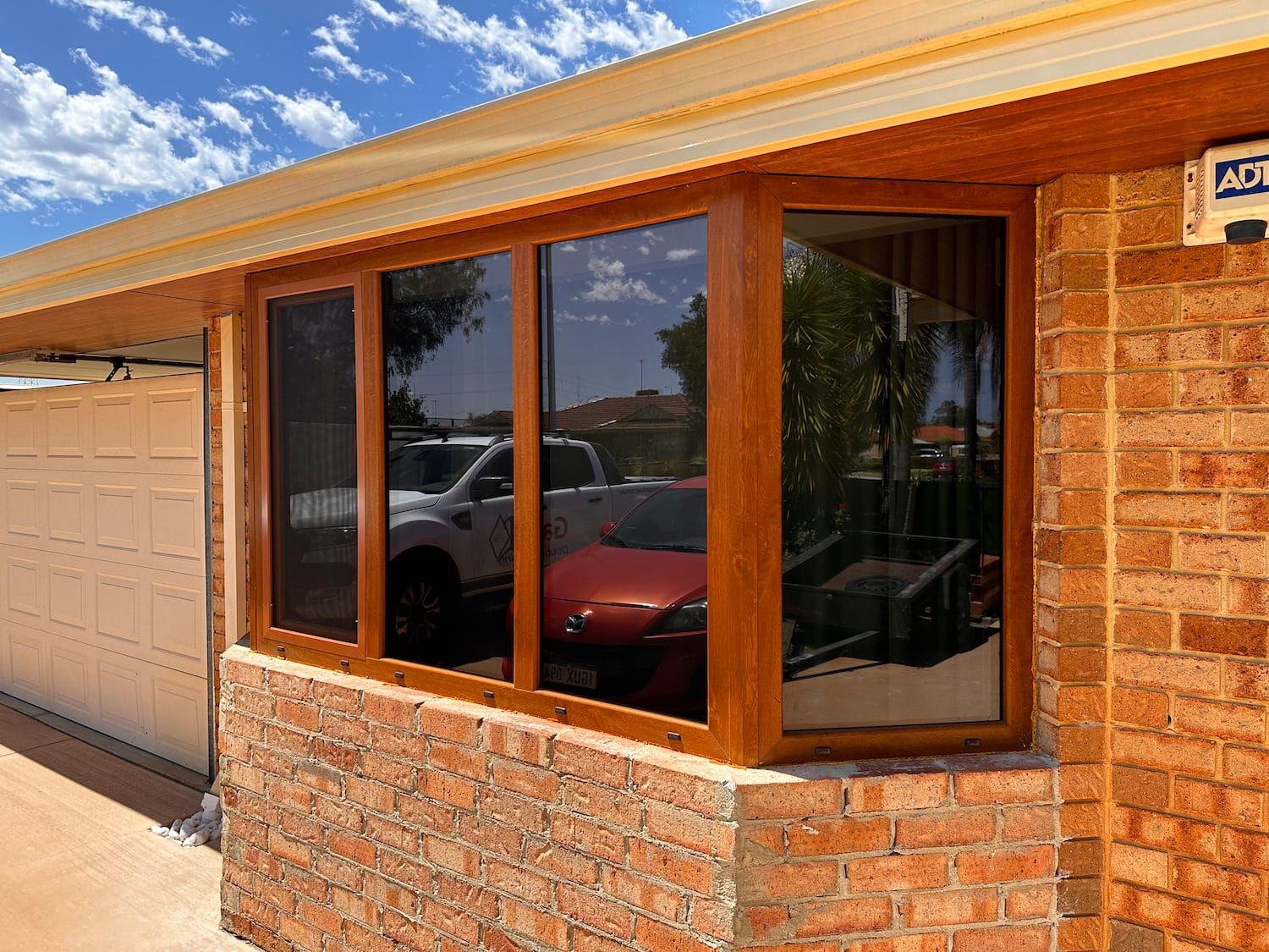 Wooden-framed bay windows on a brick home reflect parked cars. The windows are tinted.